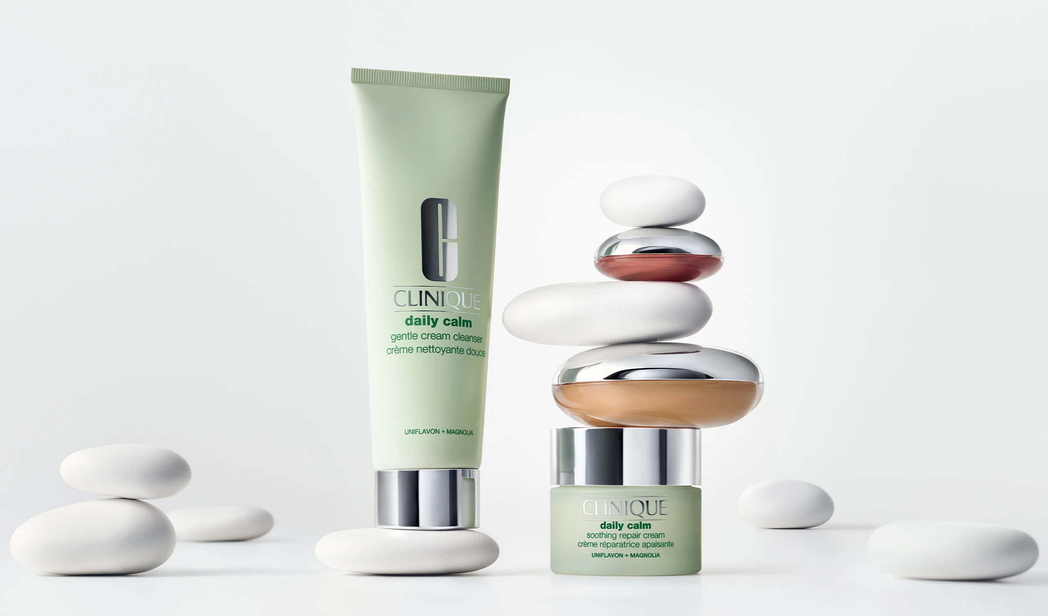 Clinique Daily Calm-rens og ansiktskrem mot lys bakgrunn ved siden av balanserte steiner. 