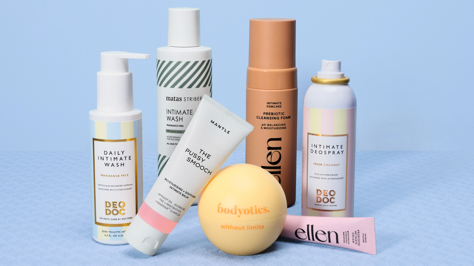 Flera intimvårdsprodukter och hudvårdsprodukter står uppställda mot ljusblå bakgrund, bland annat DeoDoc Daily Intimate Wash Fragrance Free, Matas Striber Intimate Wash, Mantle The Pussy Smooch, ellen Prebiotic Cleansing Foam, Bodyotics without limits och Intimate Deospray Fresh Coconut. Produkterna visas i pastellfärgad förpackningsdesign med synliga varumärken och texter för intimtvätt, prebiotisk rengöring, deodorant och återfuktande intimvård.