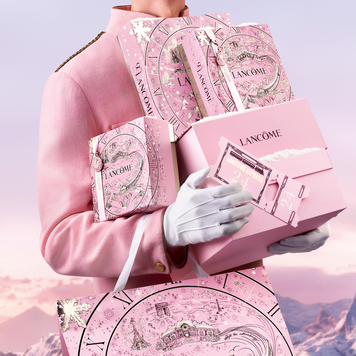 En person som håller flera rosa Lancôme-presentaskar, klädd i rosa jacka och vita handskar. I bakgrunden syns ett bergslandskap i rosa och lila nyanser.