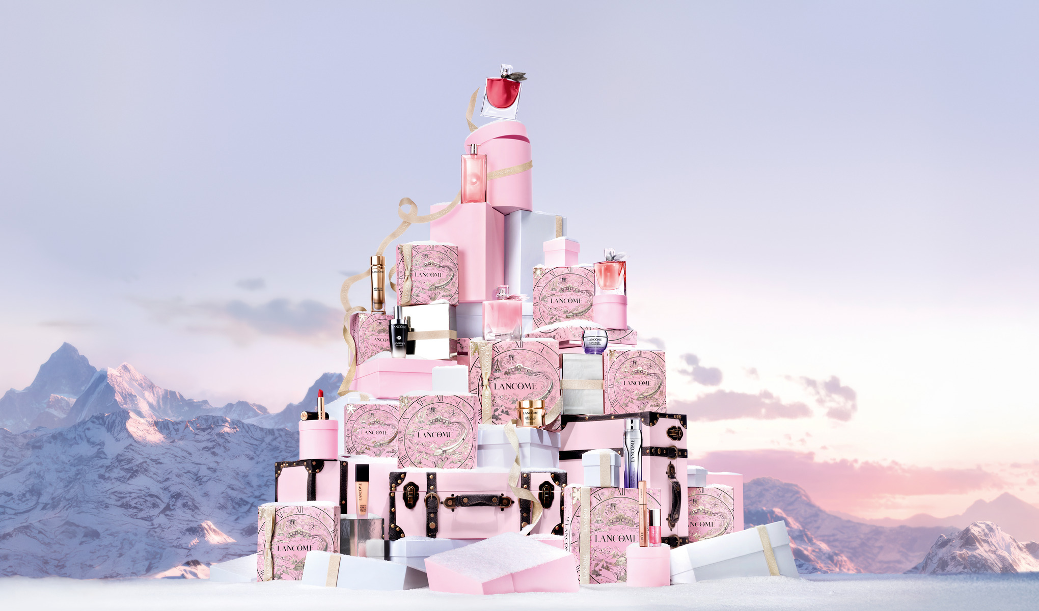 En samling Lancôme-produkter, vakkert utstilt i rosa og hvite emballasjer i et snødekt fjellandskap. I bakgrunnen skimrer fjelltoppene i rosa og lilla toner.