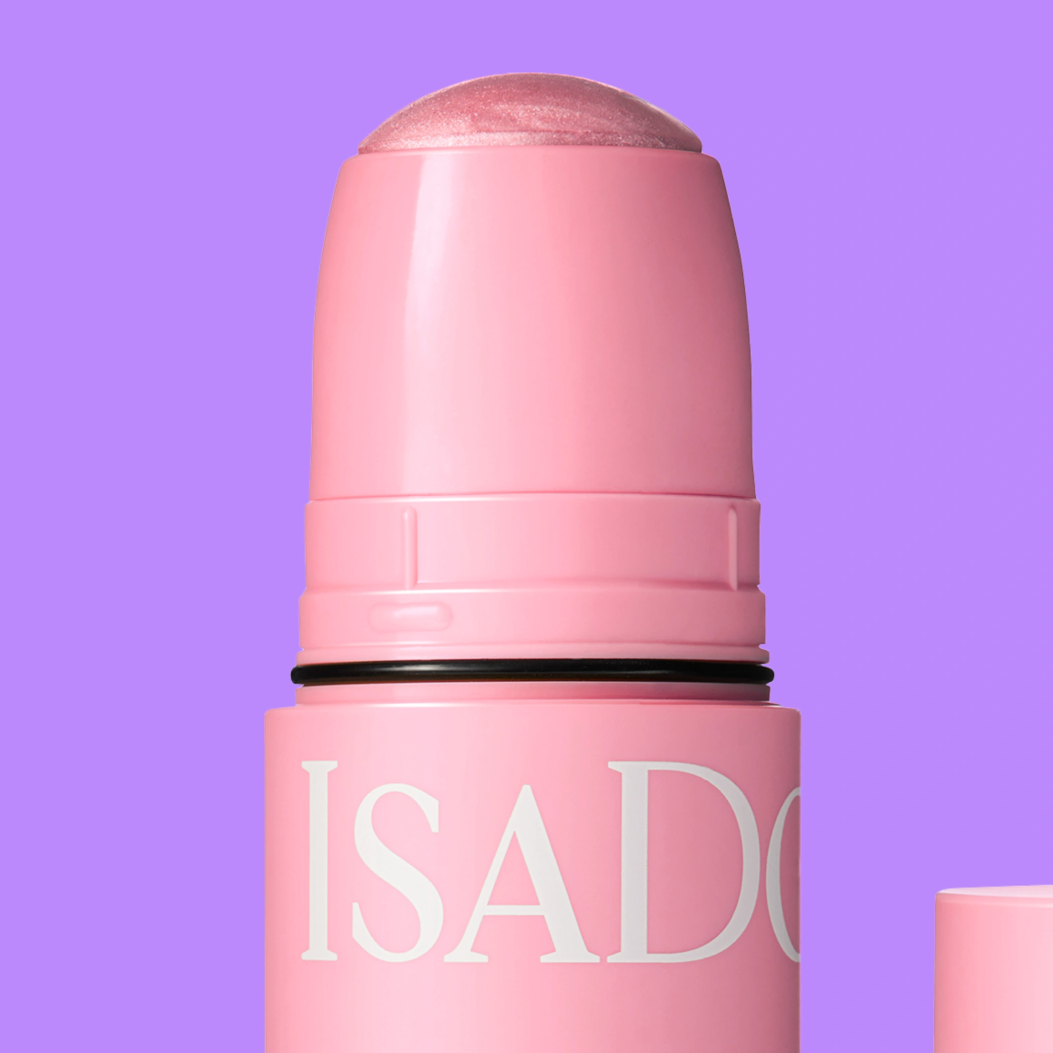 Lähikuva IsaDora The Lip & Cheek Tint Cooling Jelly Stick -puikosta vaaleanpunaisessa hylsyssä, jossa on läpikuultava sävytetty kärki, violettia taustaa vasten.