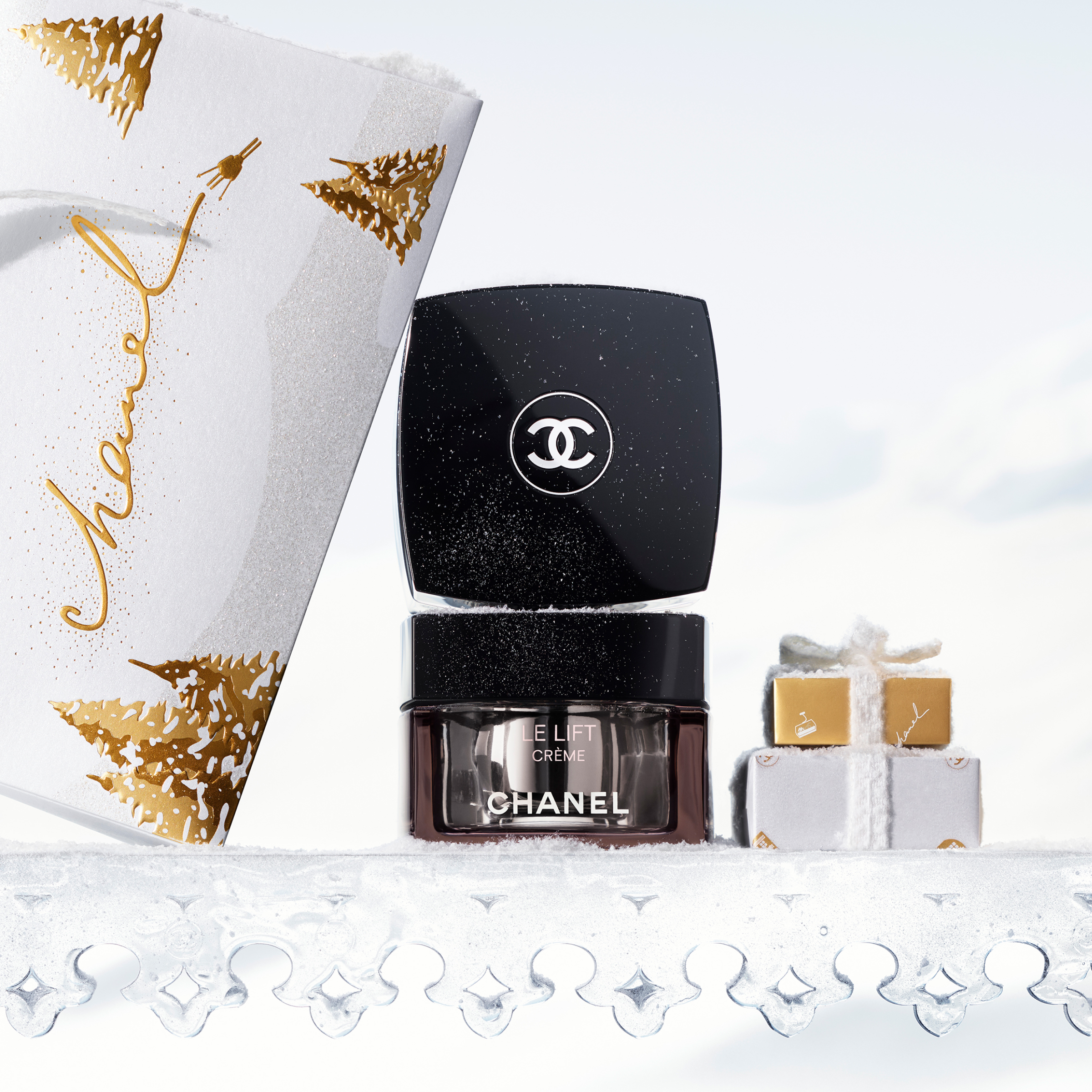 Chanel LE LIFT CRÈME krukke på snødekt overflate med festlig gaveemballasje i gull og hvitt.