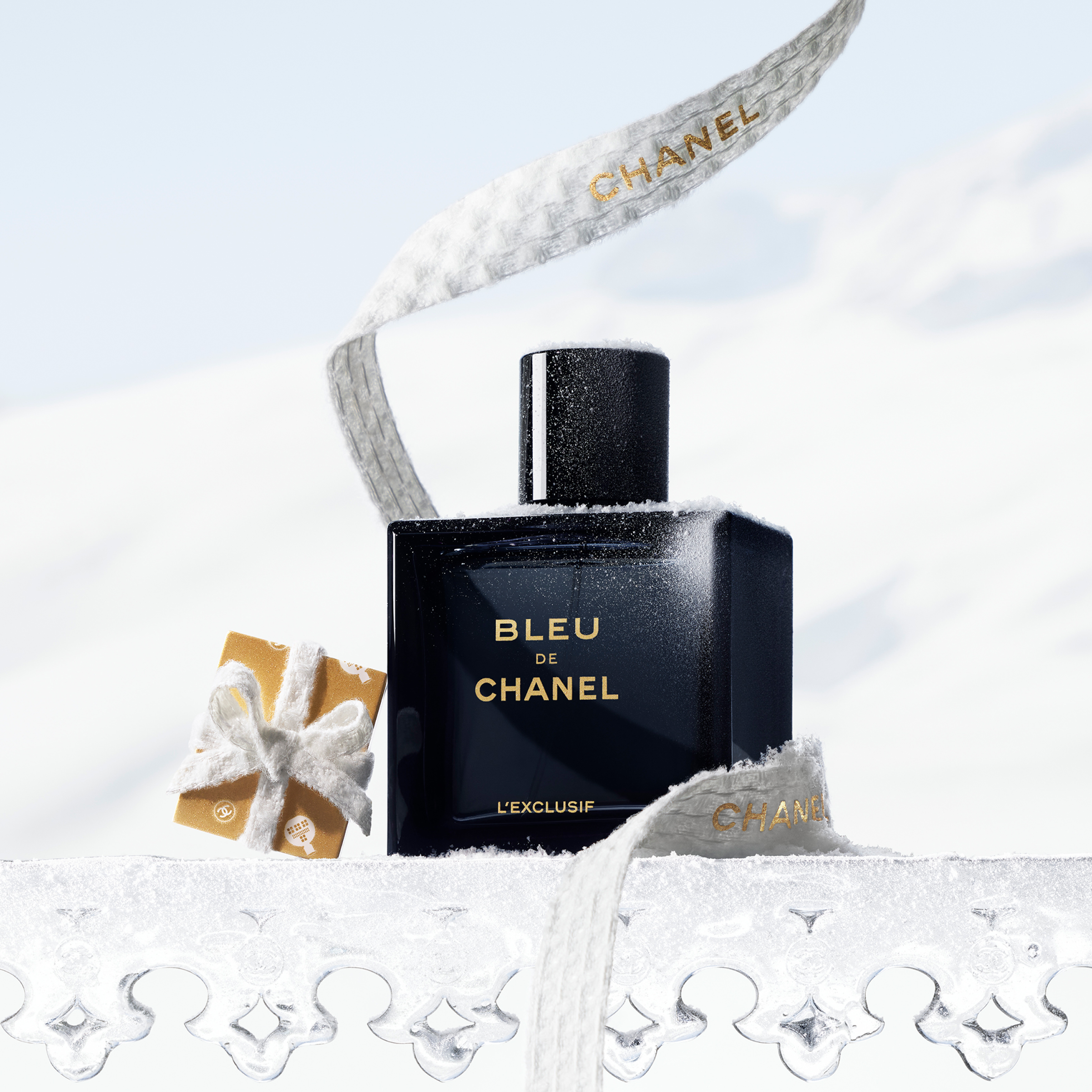 Chanel Bleu de Chanel L'Exclusif parfymeflaske og liten gaveeske på en snødekt overflate med et Chanel-bånd.