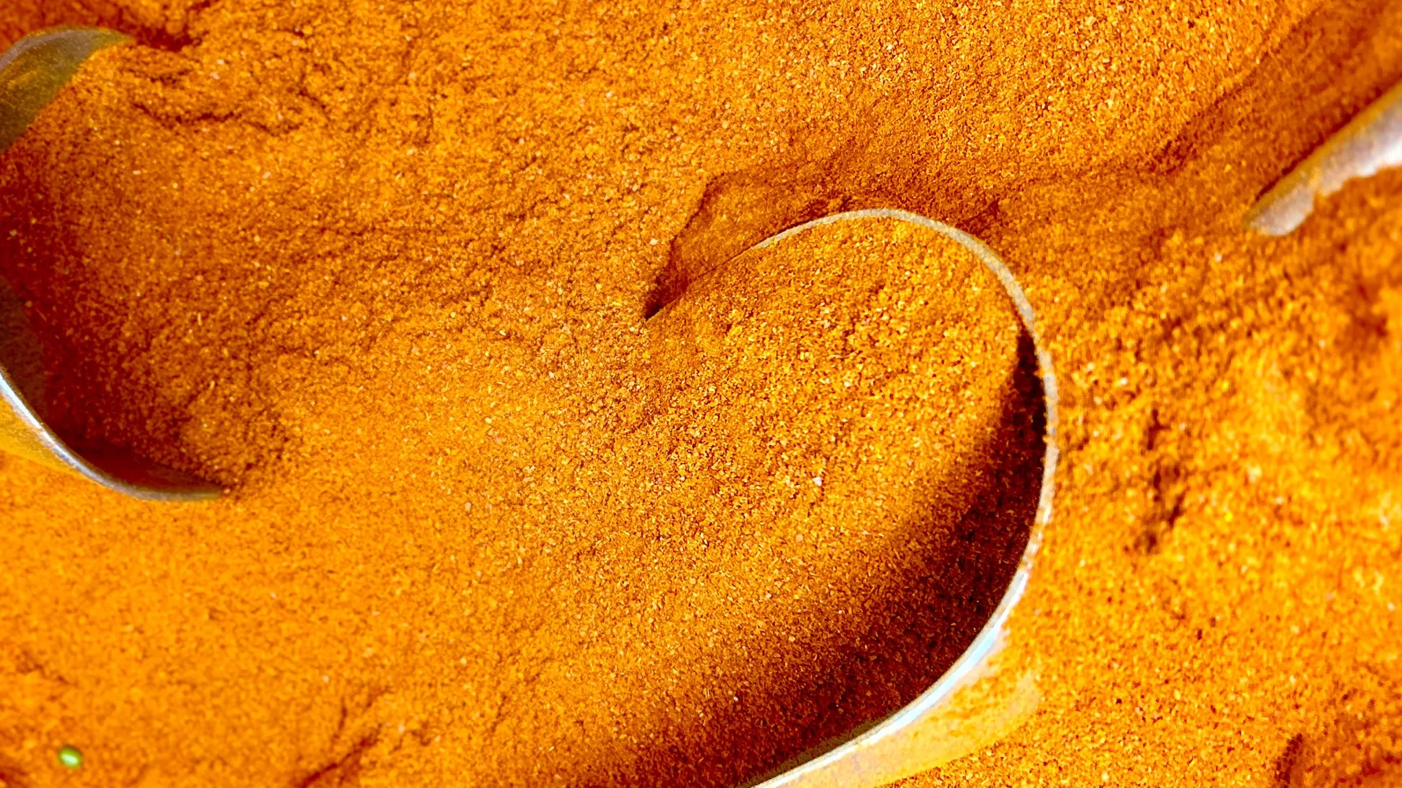 Oranssinsävyistä kurkumaa, jota nostetaan metallilusikoilla.