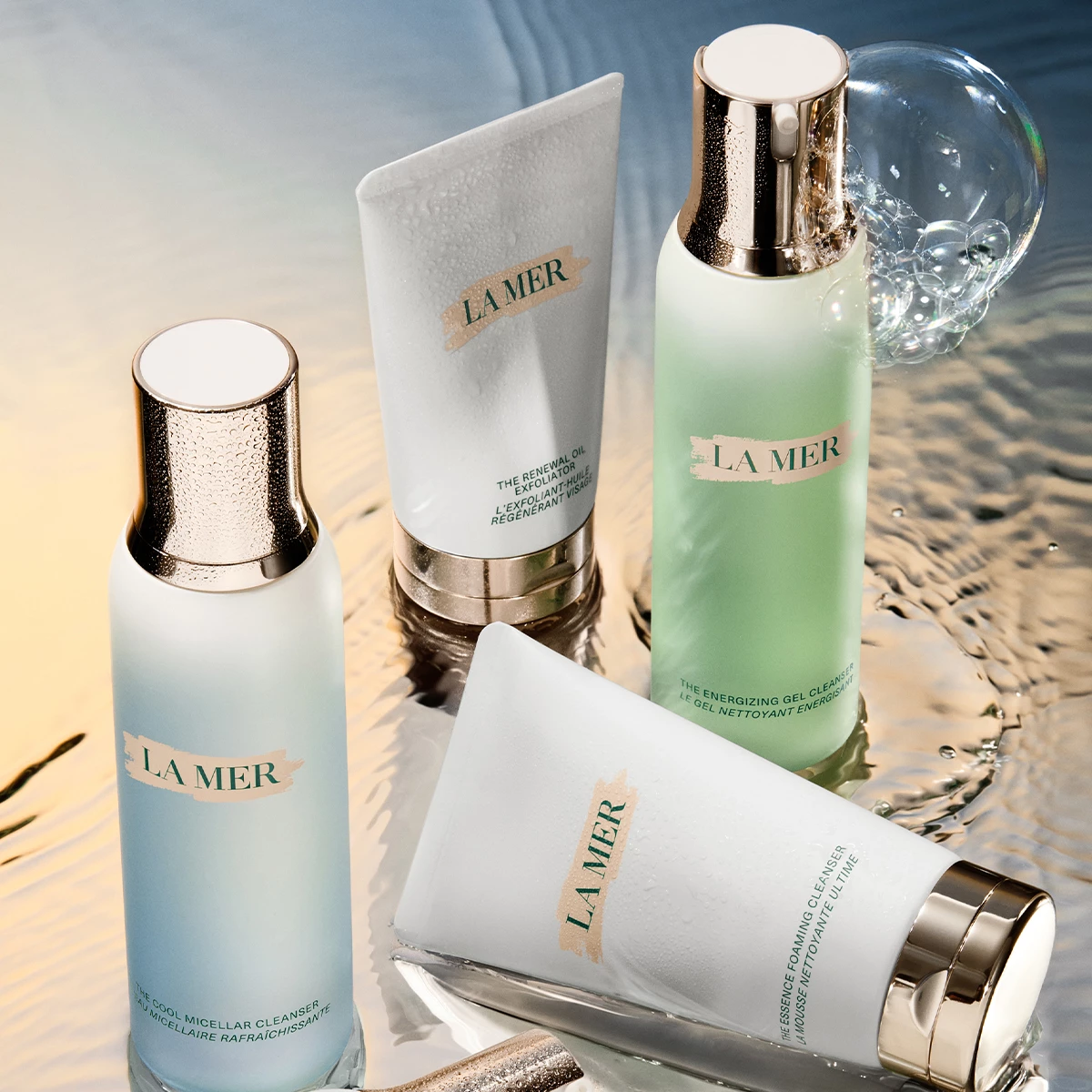 Fire La Mer hudpleieprodukter plassert på en reflekterende overflate med vann och bobler i bakgrunnen.