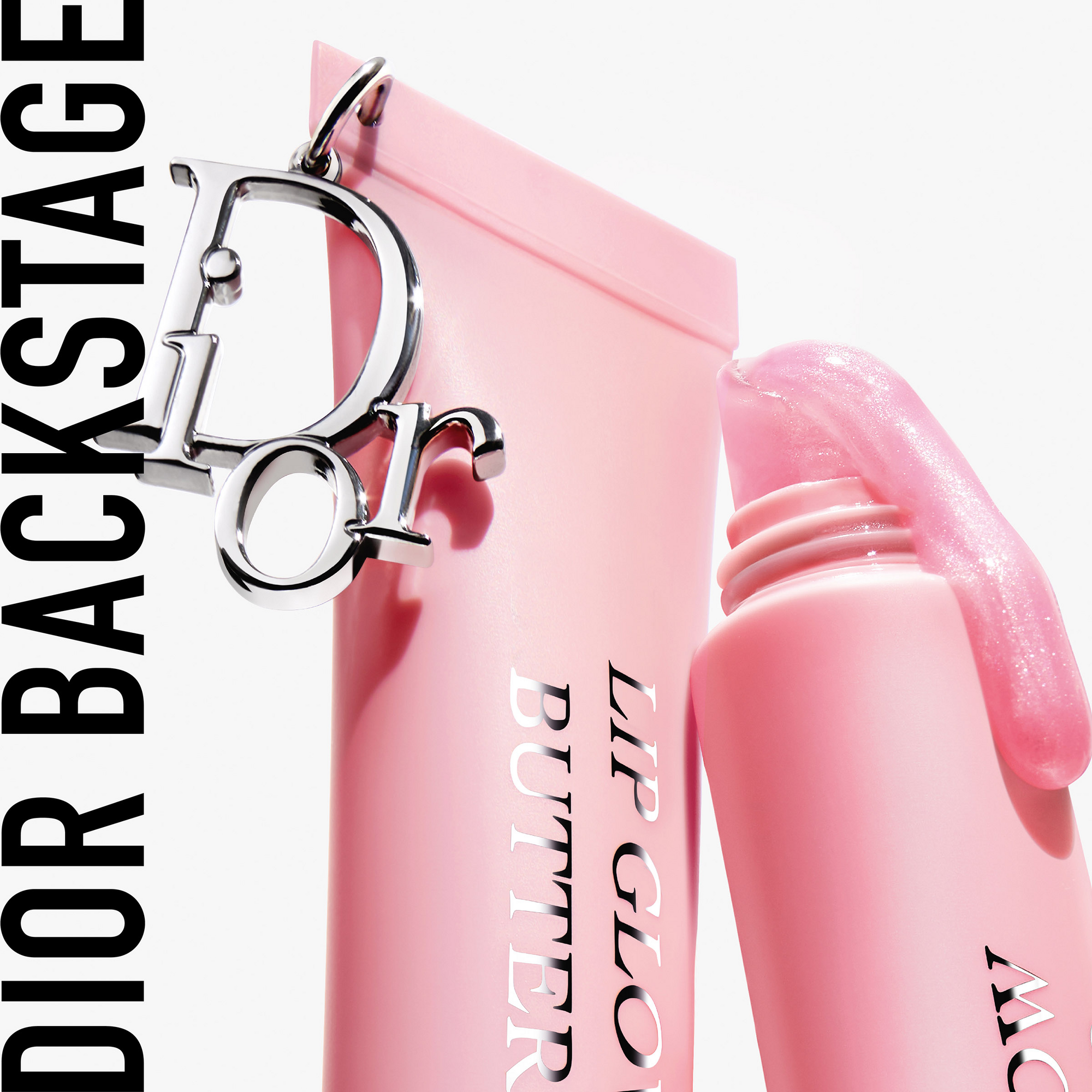 En rosa tube Dior Lip Glow Butter med et metallisk Dior-anheng er vist. Til venstre står teksten "DIOR BACKSTAGE".