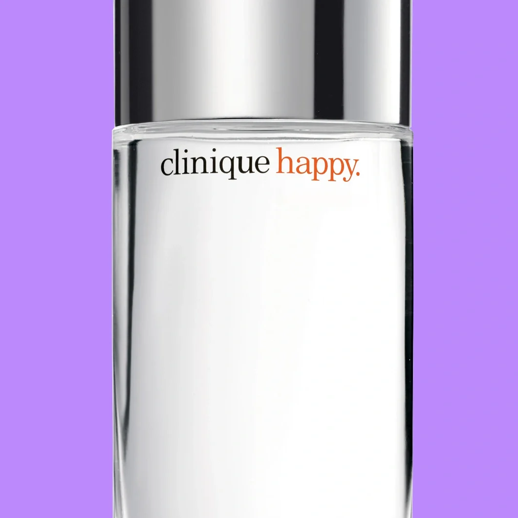 Närbild av Clinique Happy-parfym i en transparent flaska med silverfärgad kork och synlig text ”clinique happy.” mot lila bakgrund.