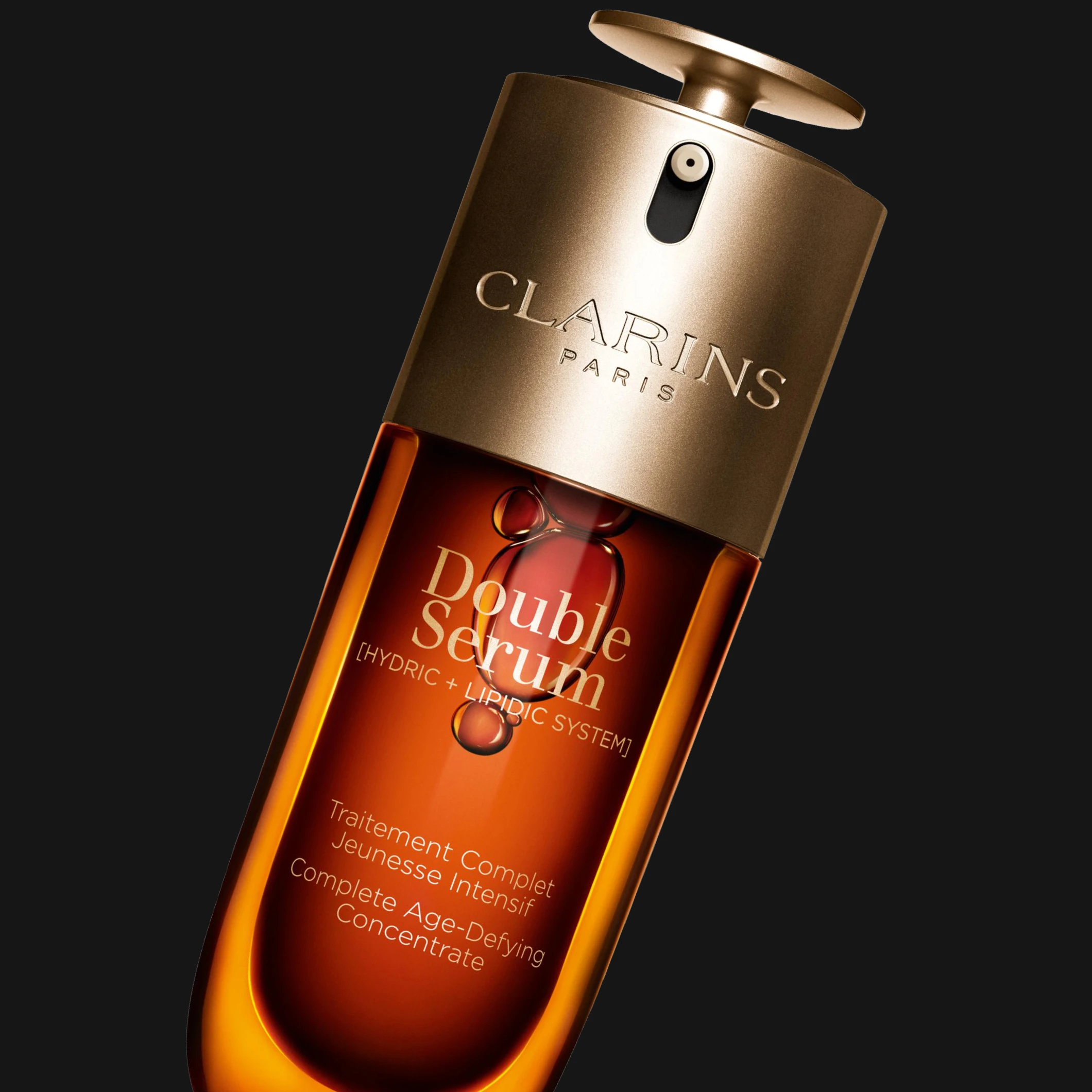 Clarins Double Serum -ihonhoitoseerumi ruskeassa ja kullanvärisessä pumppupullossa mustaa taustaa vasten. Näkyvä teksti sisältää “CLARINS PARIS”, “Double Serum”, “[HYDRIC + LIPIDIC SYSTEM]” ja “Complete Age-Defying Concentrate”.