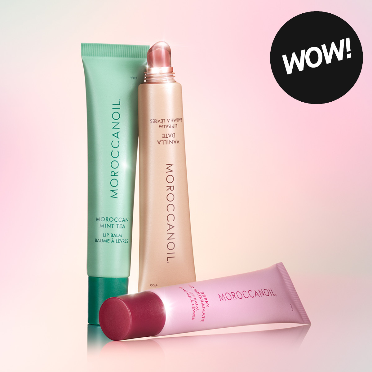 Leppeprodukter fra Moroccanoil med teksten “MOROCCANOIL”, “Moroccan Mint Tea Lip Balm”, “Vanilla Date Lip Balm” og “Berry Pomegranate Lip Balm”. Tre fargede leppebalmer i tuber vises mot en rosa bakgrunn sammen med en rund etikett med teksten “WOW!”.