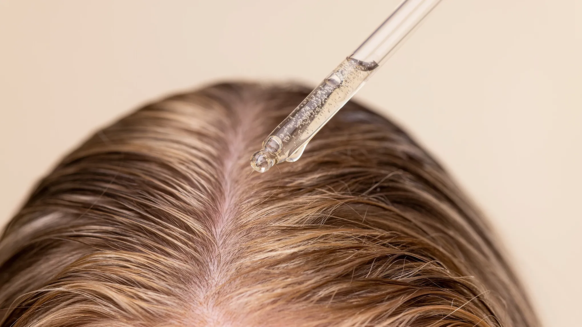 Serum dryppes på hodebunnen foran en beige bakgrunn.