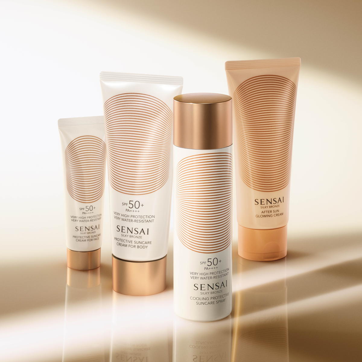 Fyra solskyddsprodukter från SENSAI Silky Bronze står uppställda mot en varm beige bakgrund: Protective Suncare Cream for Face SPF 50+ PA++++, Protective Suncare Cream for Body SPF 50+ PA++++, Cooling Protective Suncare Spray SPF 50+ och After Sun Glowing Cream. Produkterna har vit och gyllene design och förmedlar premium solskydd, sunscreen och after sun för ansikte och kropp.