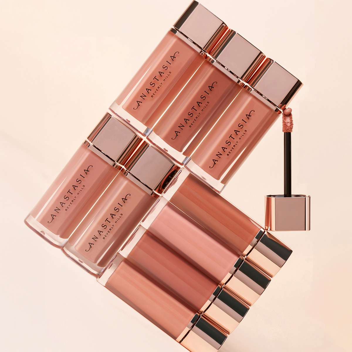 Kuva kahdeksasta Anastasia Beverly Hillsin huulikiiltokuidusta, jotka on järjestetty geometriseen kuvioon vaaleanpunaisen ja nuden eri sävyissä. Yksi huulikiiltoaplikaattoreista on pidennetty ja näkyvissä.