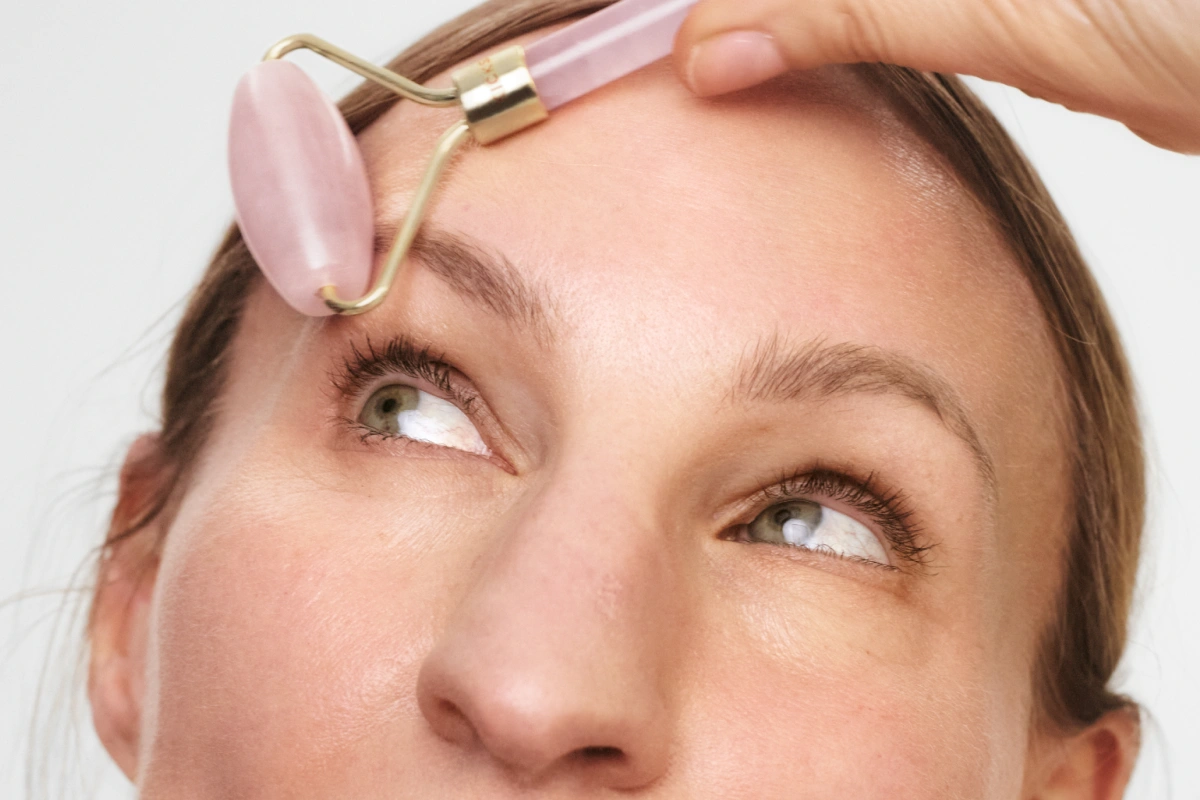 Person bruker en rosa jade roller på pannen for ansiktsmassasje, med fokus på hudpleie og glød.