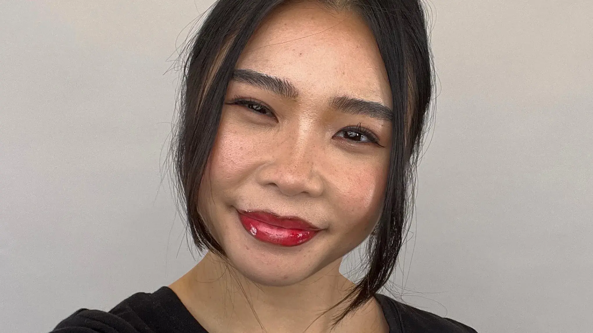 Närbild på en leende person med cherry cola-läppar – en trendig makeupstil med mörkare läppkontur och glansigt rött läppstift.