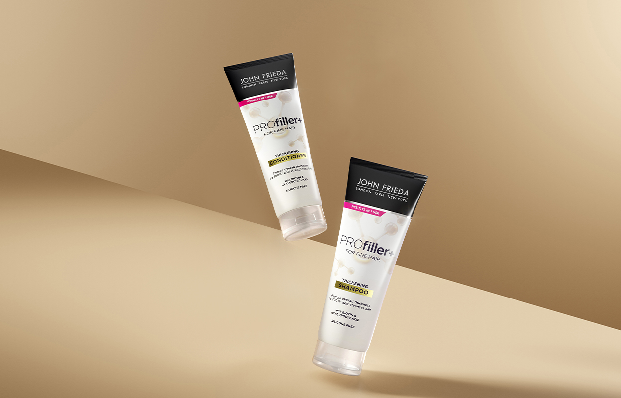 Kaksi hiustenhoitotuotetta John Friedalta, hoitoaine ja shampoo, molemmat sarjasta ”PROfiller+ for Fine Hair”. Tuotteet on sijoitettu beigeä taustaa vasten.