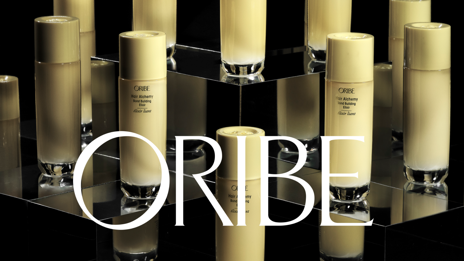 Flere Oribe Hair Alchemy Bond Building Elixir-flasker på reflekterende svarte overflater. Stor hvit tekst 'ORIBE' overlagt.