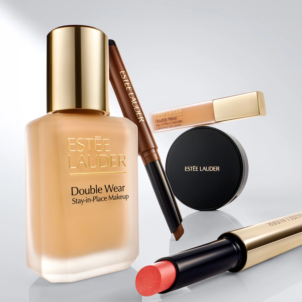 Estée Lauder -meikit: Double Wear Stay-in-Place Makeup -meikkivoide, Double Wear Stay-in-Place Concealer Correcteur anti-cernes -peitevoide, rajauskynä, puuterirasia ja korallinpunainen huulipuna.