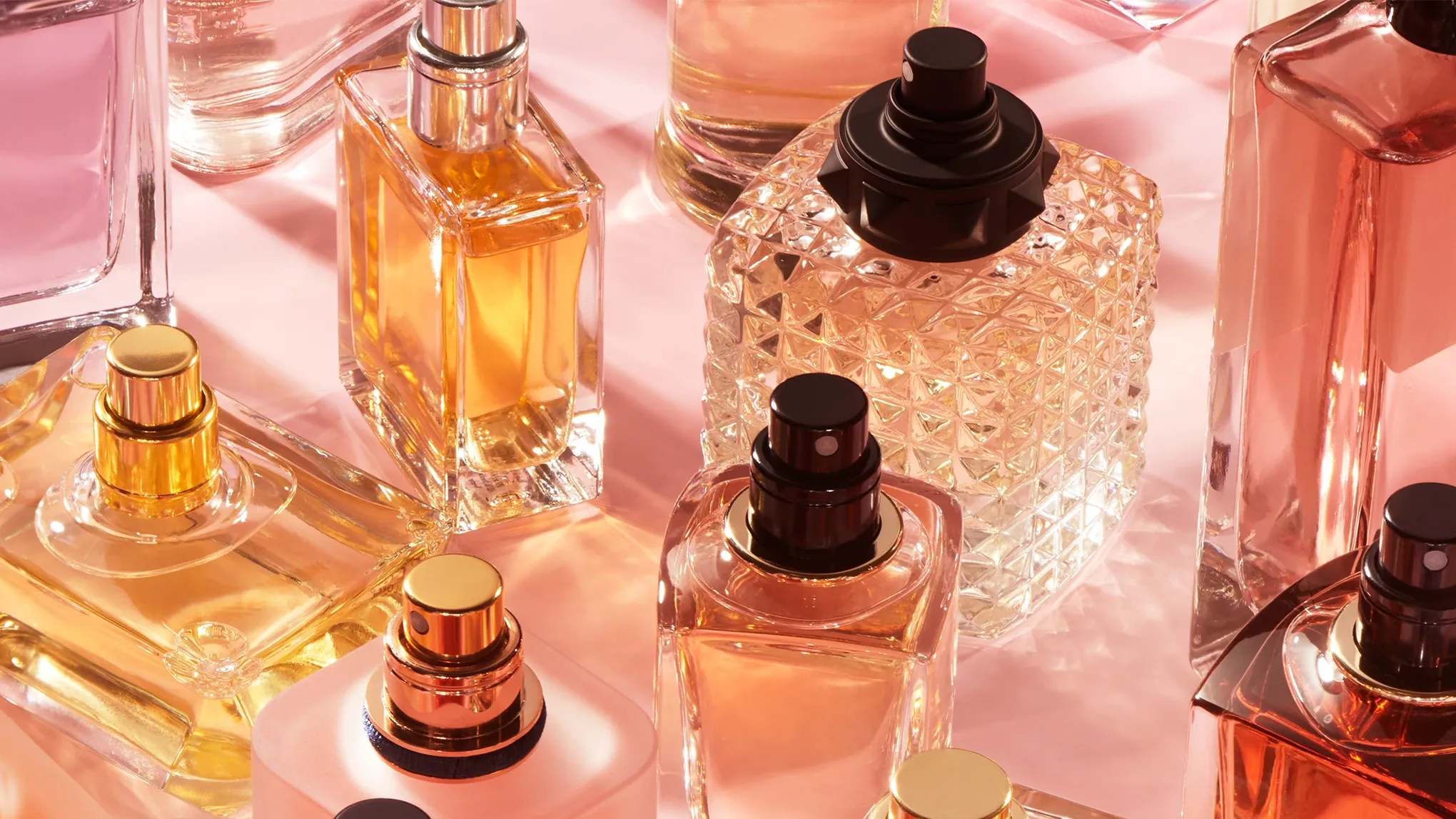 Vakre parfymeflasker i ulike former og farger på rosa bakgrunn