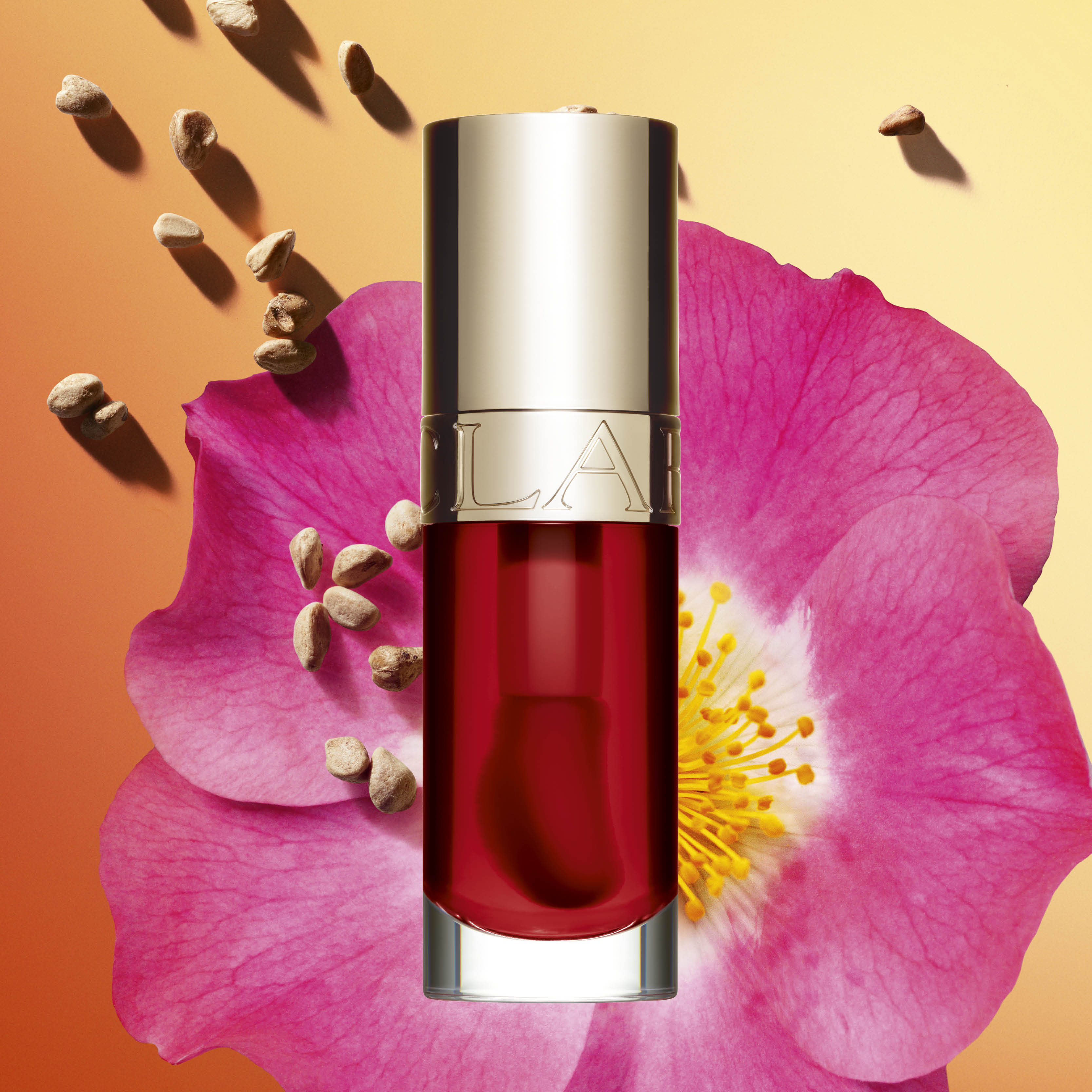 Produktflaska från Clarins med röd vätska, placerad framför en stor rosa blomma och små frön mot en orange bakgrund.