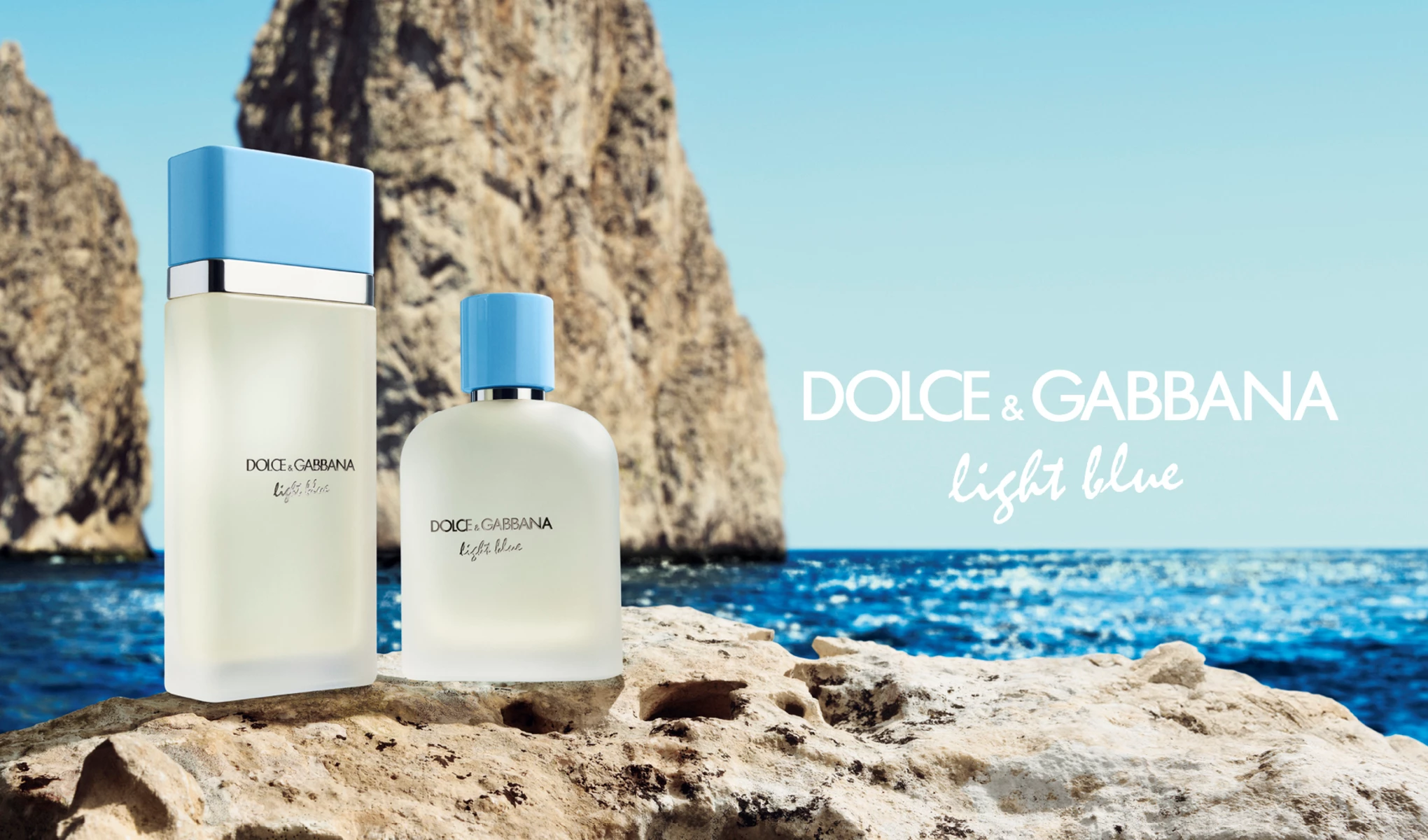 Kaksi Dolce & Gabbana Light Blue -hajuvesipulloa seisoo kivellä sinisen meren edessä, taustalla kallioita. Pulloissa on vaaleansiniset korkit ja minimalistinen muotoilu.