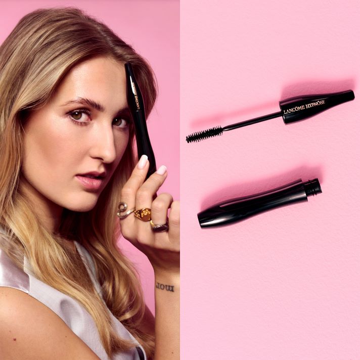 En person holder en Lancôme Hypnôse mascara nær ansiktet mot rosa bakgrunn, ved siden av vises børste og hylse separert.
