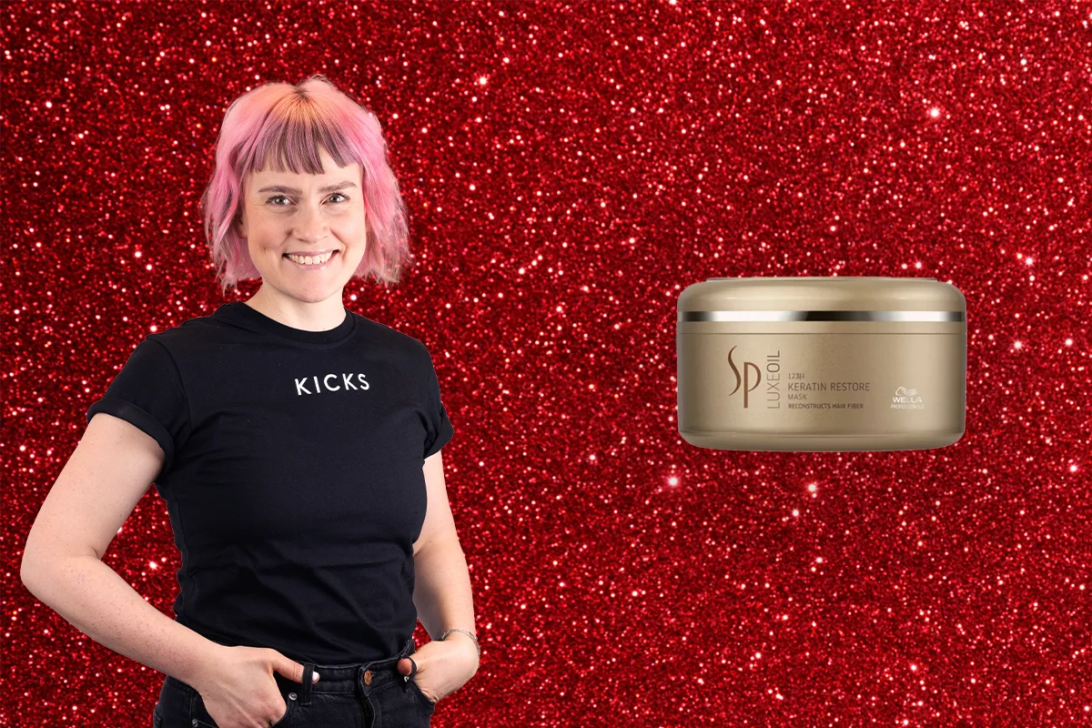 En person med rosa hår i en svart KICKS-tröja står framför en röd glittrande bakgrund bredvid en burk med SP hårmask.