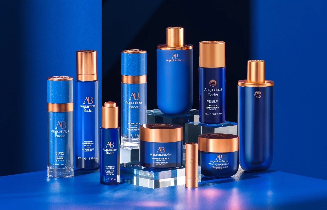 Hudpleieprodukter fra Augustinus Bader, blant annet kremer, serum og renseprodukter. Produktene er i blå emballasje med gullfargede detaljer og er plassert på en blå bakgrunn.