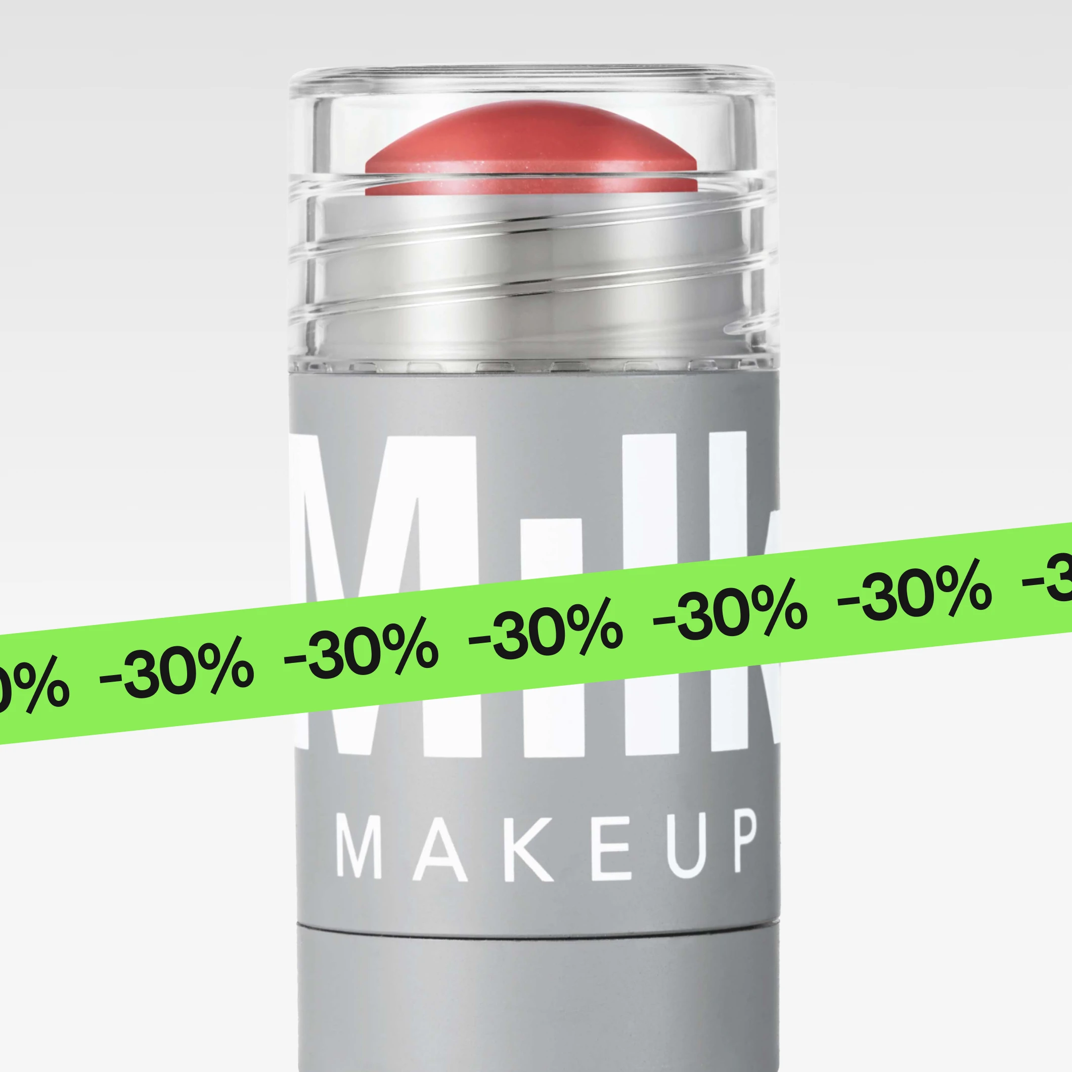 Vaaleanharmaassa pakkauksessa oleva korallinsävyinen Milk Makeup -meikkistick on kuvattu vaaleanharmaata taustaa vasten. Kuvan alaosassa näkyy vihreä banneri, jossa toistuu teksti “30%”, ja pakkauksessa lukee MILK MAKEUP.