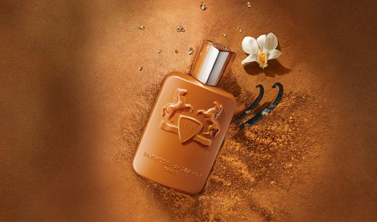 Parfums de Marly Paris -yhtiön ruskea hajuvesipullo ruskealla jauhemaisella pohjalla. Pullon vieressä on valkoinen orkideakukka ja kaksi vaniljatankoa.