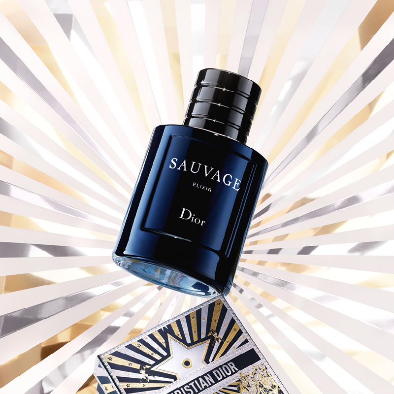 En blå Sauvage Elixir Dior-flaska, med en bakgrund av strålande linjer i guld, rosa och vitt, samt en Christian Dior-presentförpackning.