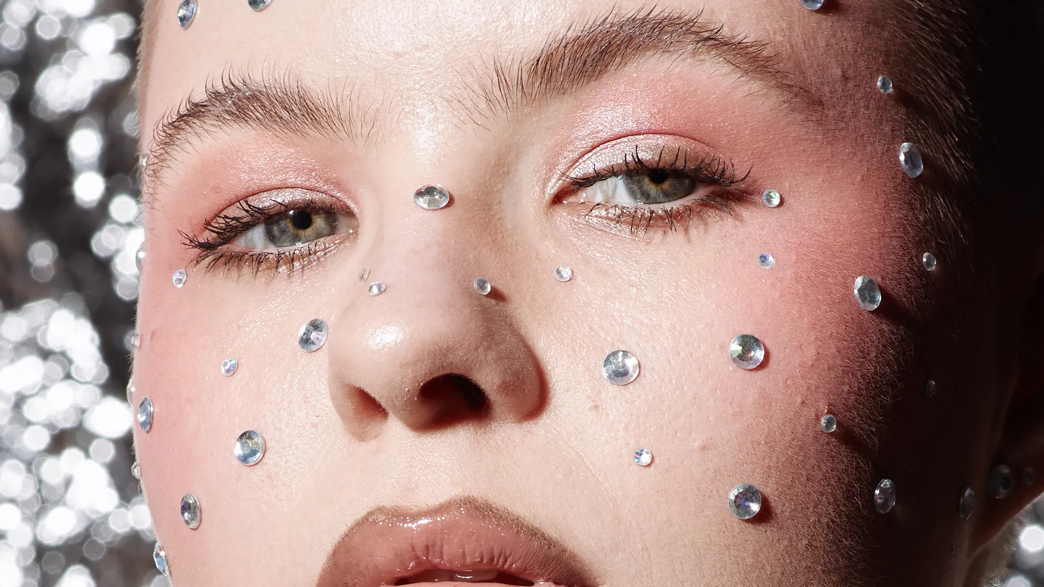 Kvinne med naturlig sminke, maskara og rhinestones rundt ansiktet som fregner.