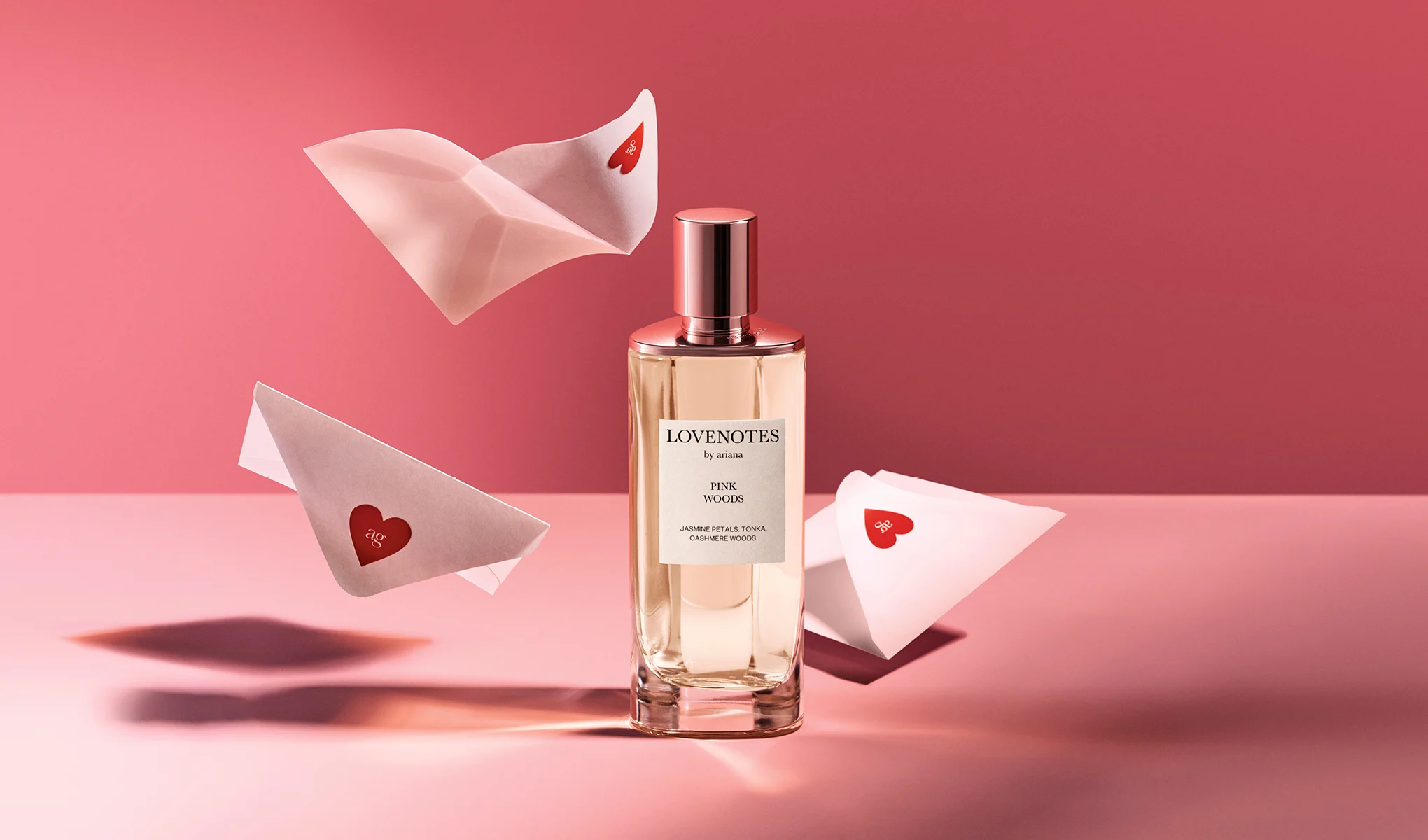 Lovenotes by Ariana Pink Woods-parfyme mot rosa bakgrunn, omgitt av konvolutter.