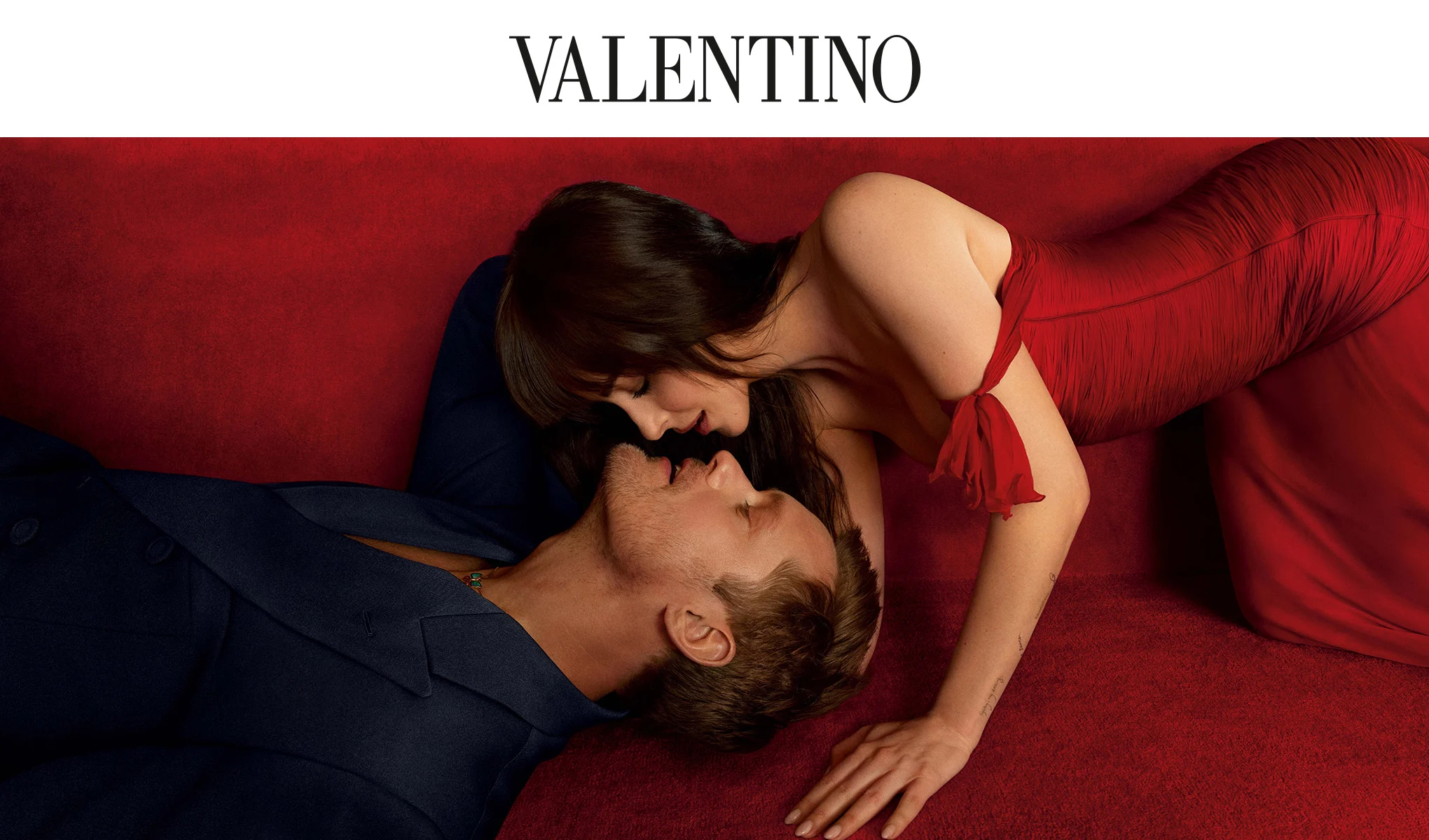Ett par ligger nära varandra på en röd soffa i en Valentino Vendetta-kampanj.