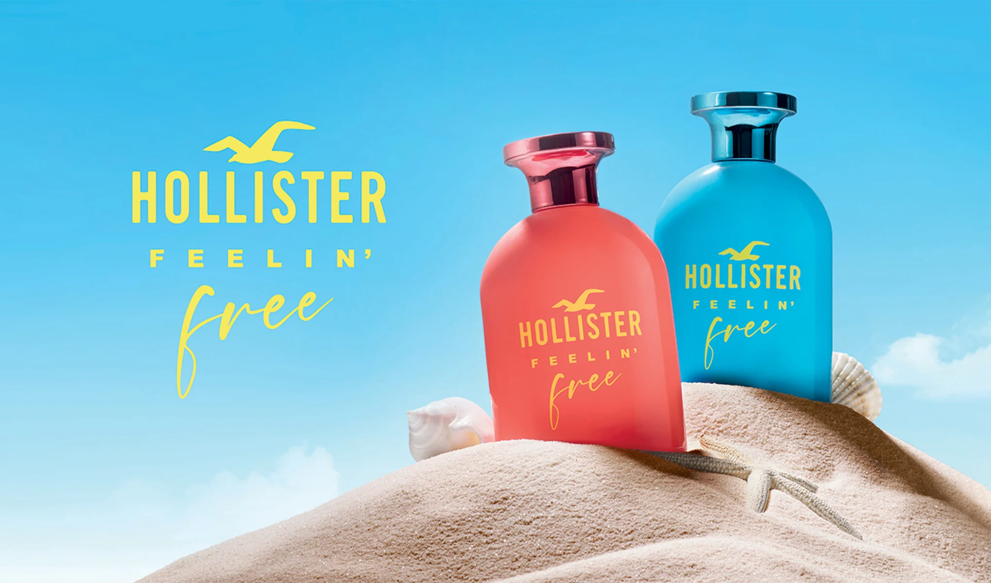 Två parfymflaskor från Hollister, en röd och en blå, placerade på en sanddyna med snäckor och en sjöstjärna. Bakgrunden är en klarblå himmel med texten "Hollister Feelin' Free" i gult.