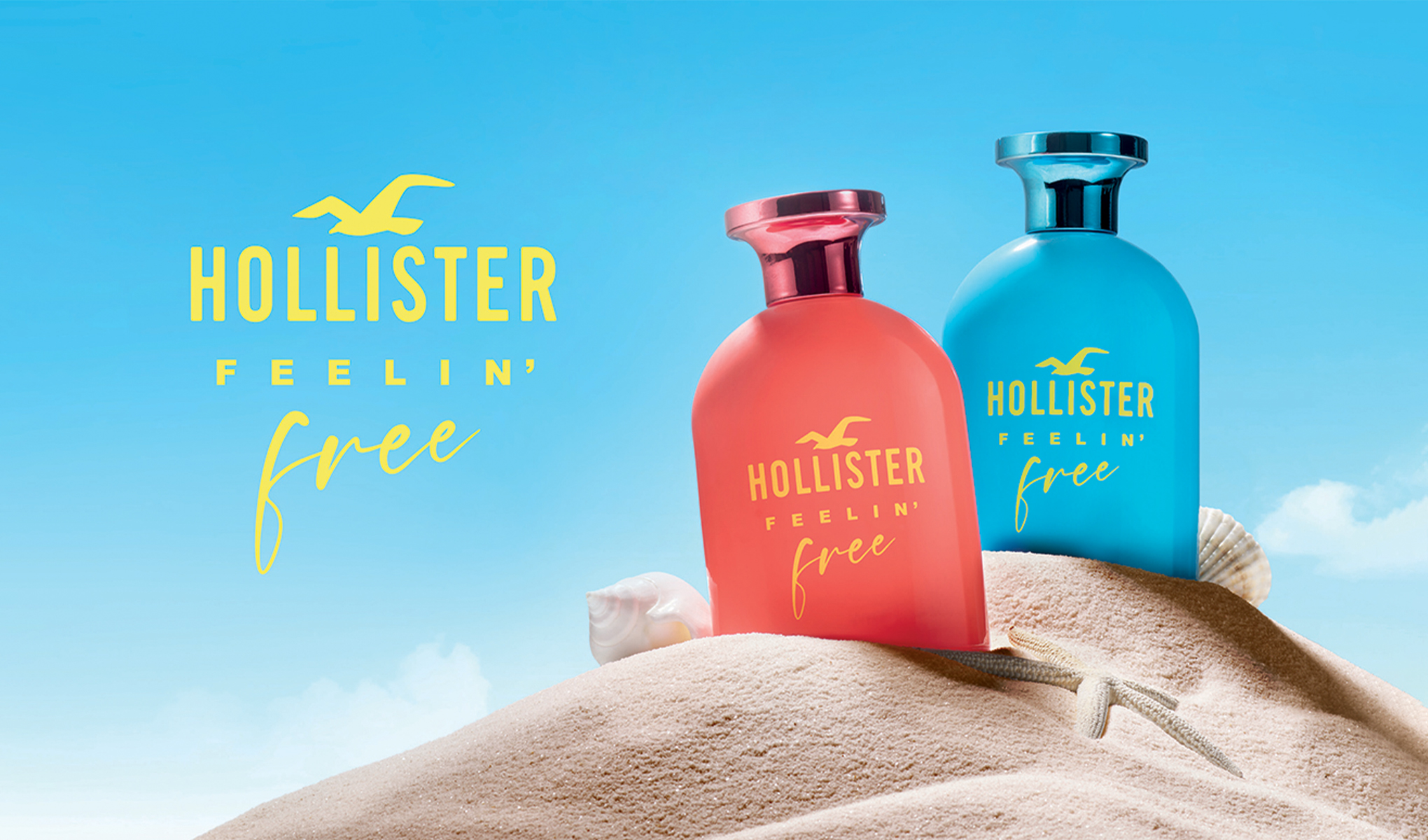 Kaksi Hollisterin hajuvesipulloa, yksi punainen ja yksi sininen, sijoitettu hiekkadyynille, jossa on simpukoita ja meritähti. Taustalla on kirkkaansininen taivas ja keltaisella teksti ”Hollister Feelin' Free”.