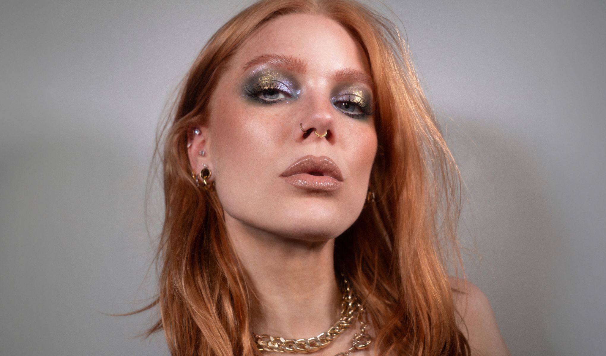 Punahiuksinen henkilö, jolla on kultaisia koruja ja useita korvakoruja.
