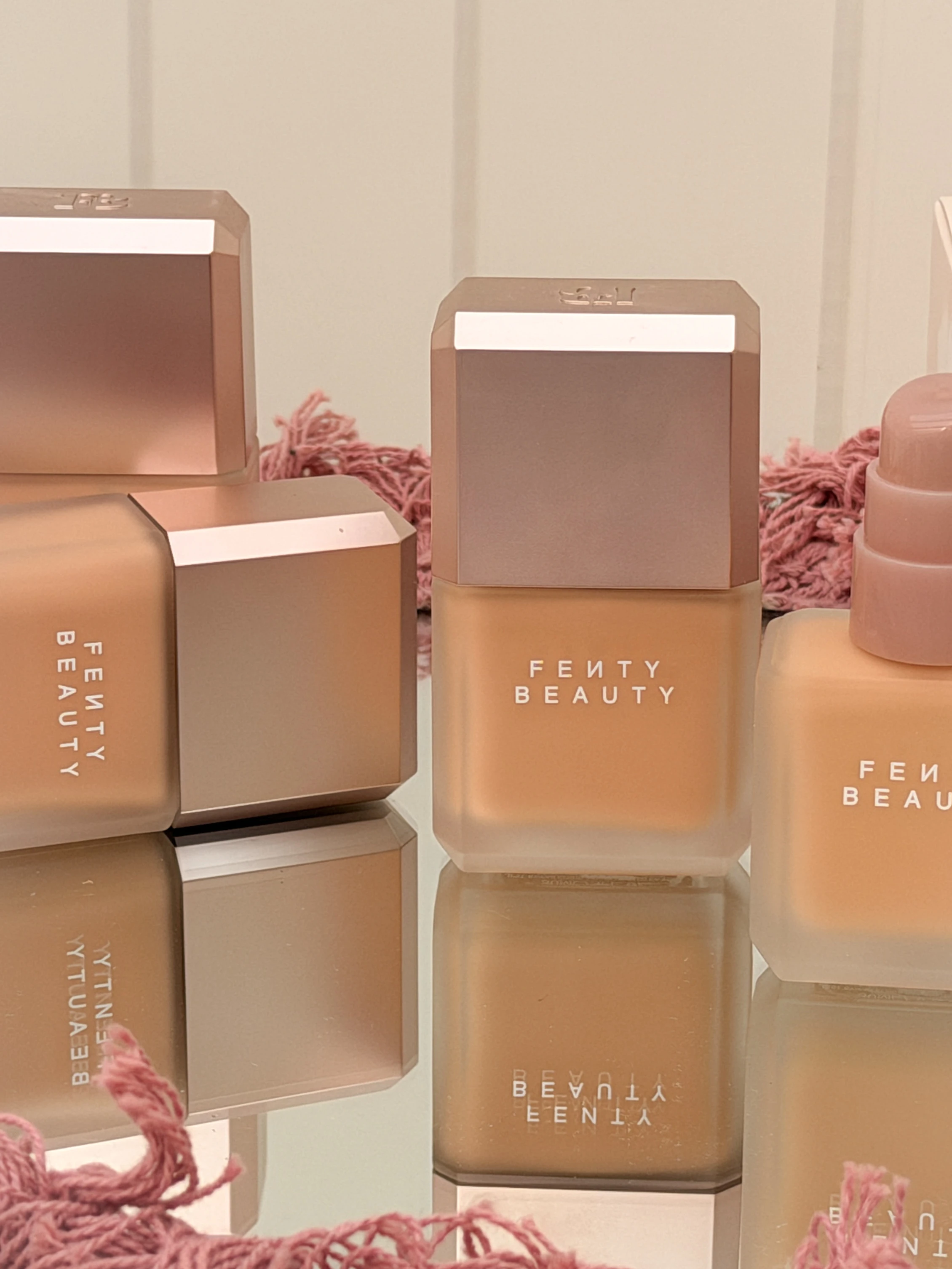 Fenty Beauty foundationflasker med rosaguld låg og 'FENTY BEAUTY'-branding, på en reflekterende overflade.