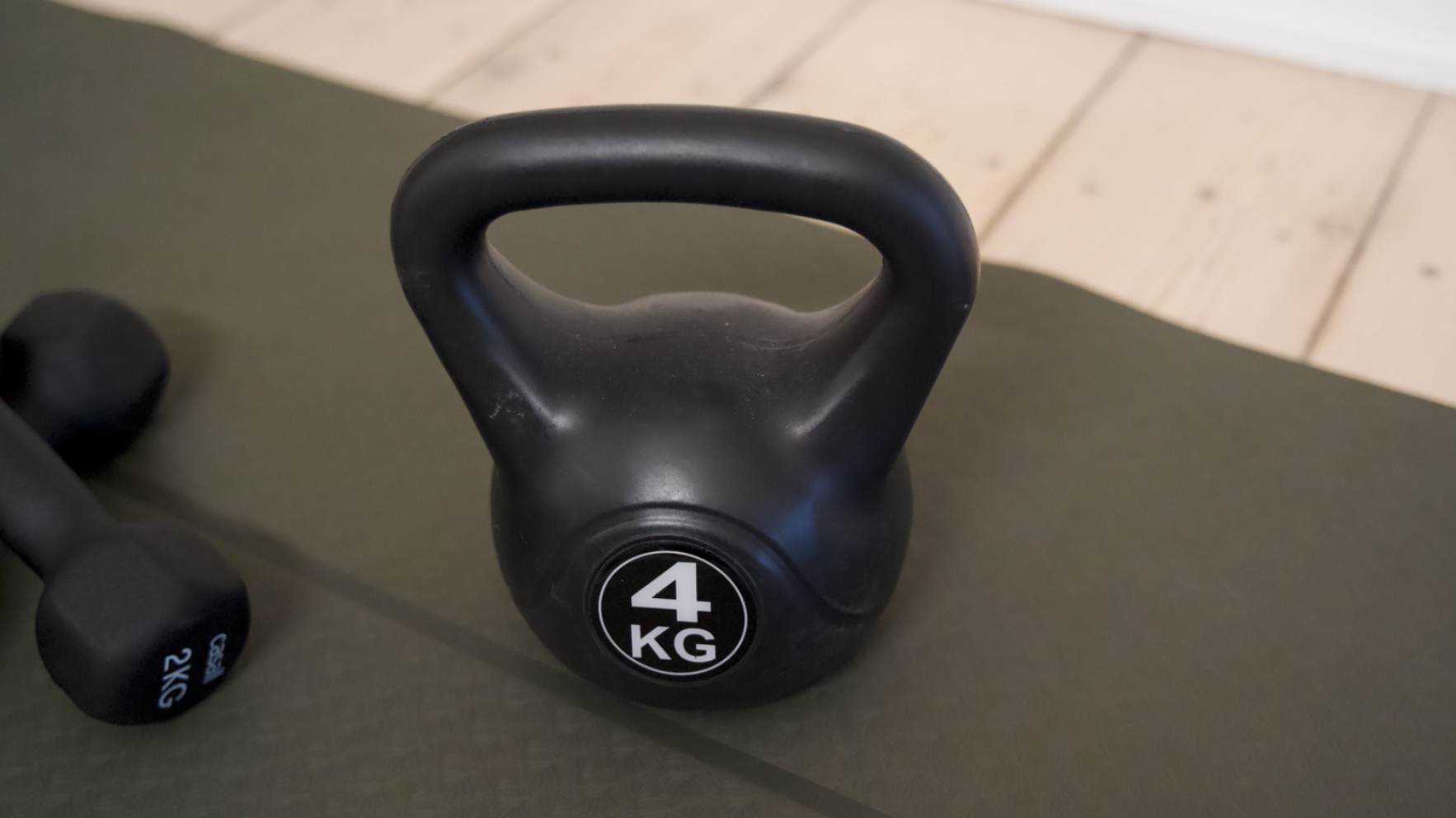 En sort 4 KG kettlebell og en sort 2 KG Casall håndvægt på en mørkegrøn yogamåtte.