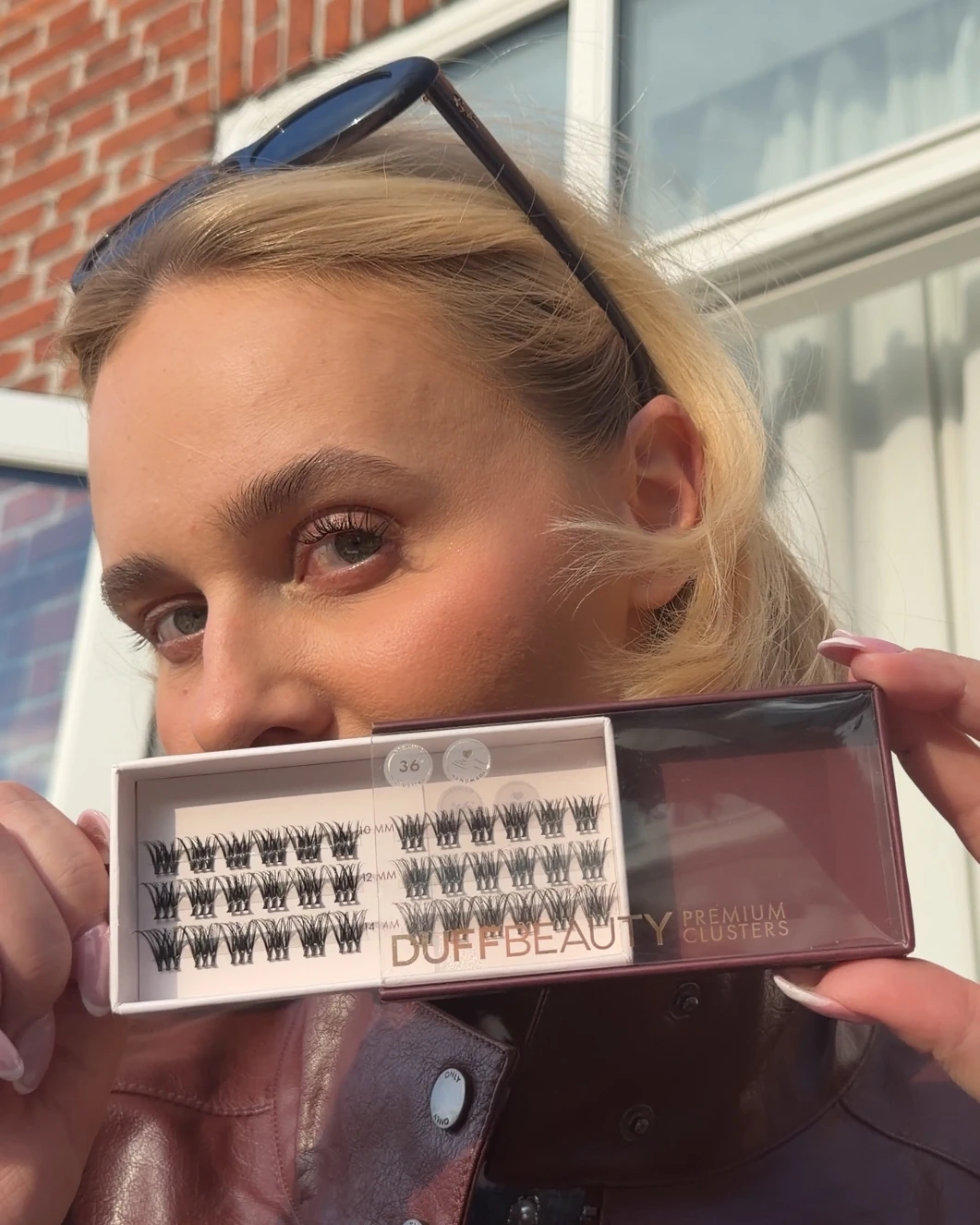 En person holder en åben æske med Duffbeauty Premium Clusters, der viser 36 falske øjenvippeklynger i 10 mm, 12 mm og 14 mm længder.