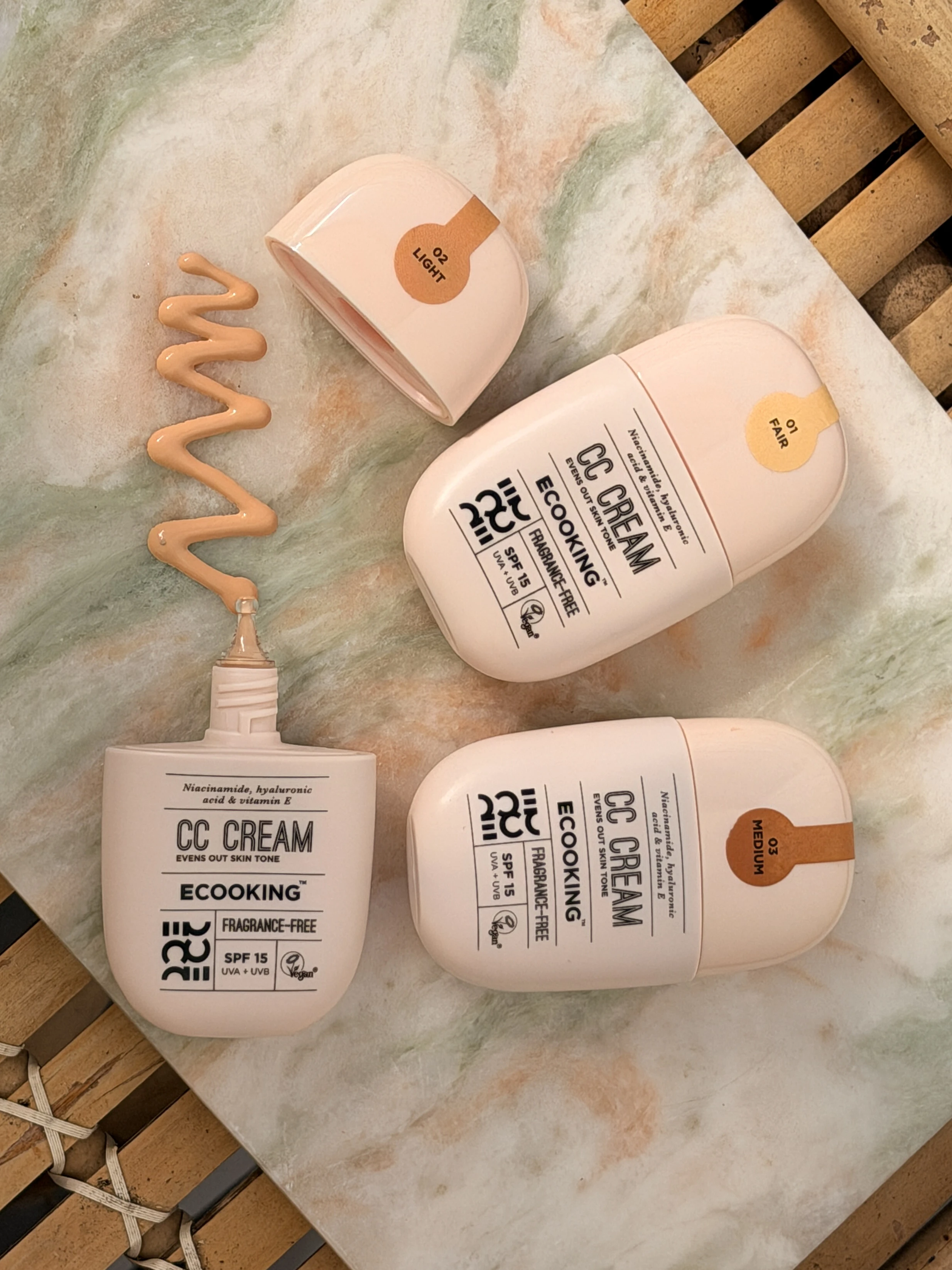 Ecooking CC Cream i nuancerne 01 Fair, 02 Light og 03 Medium. Udjævner hudtonen, parfumefri, vegansk, SPF 15, med niacinamid, hyaluronsyre og vitamin E. En stribe creme er presset ud.