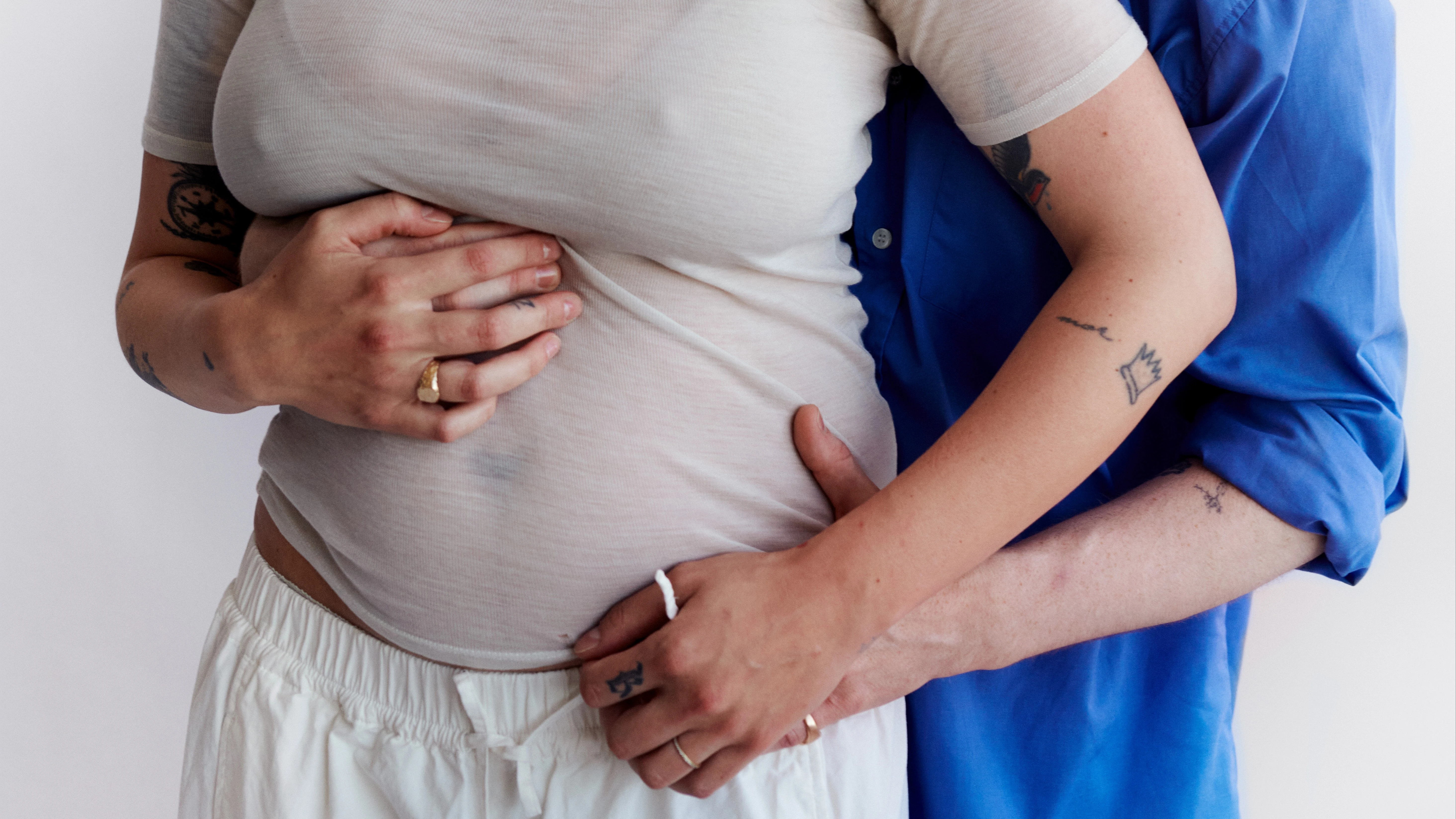 Et smilende par i en omfavnelse, hvor den ene person er gravid og den anden holder om maven.