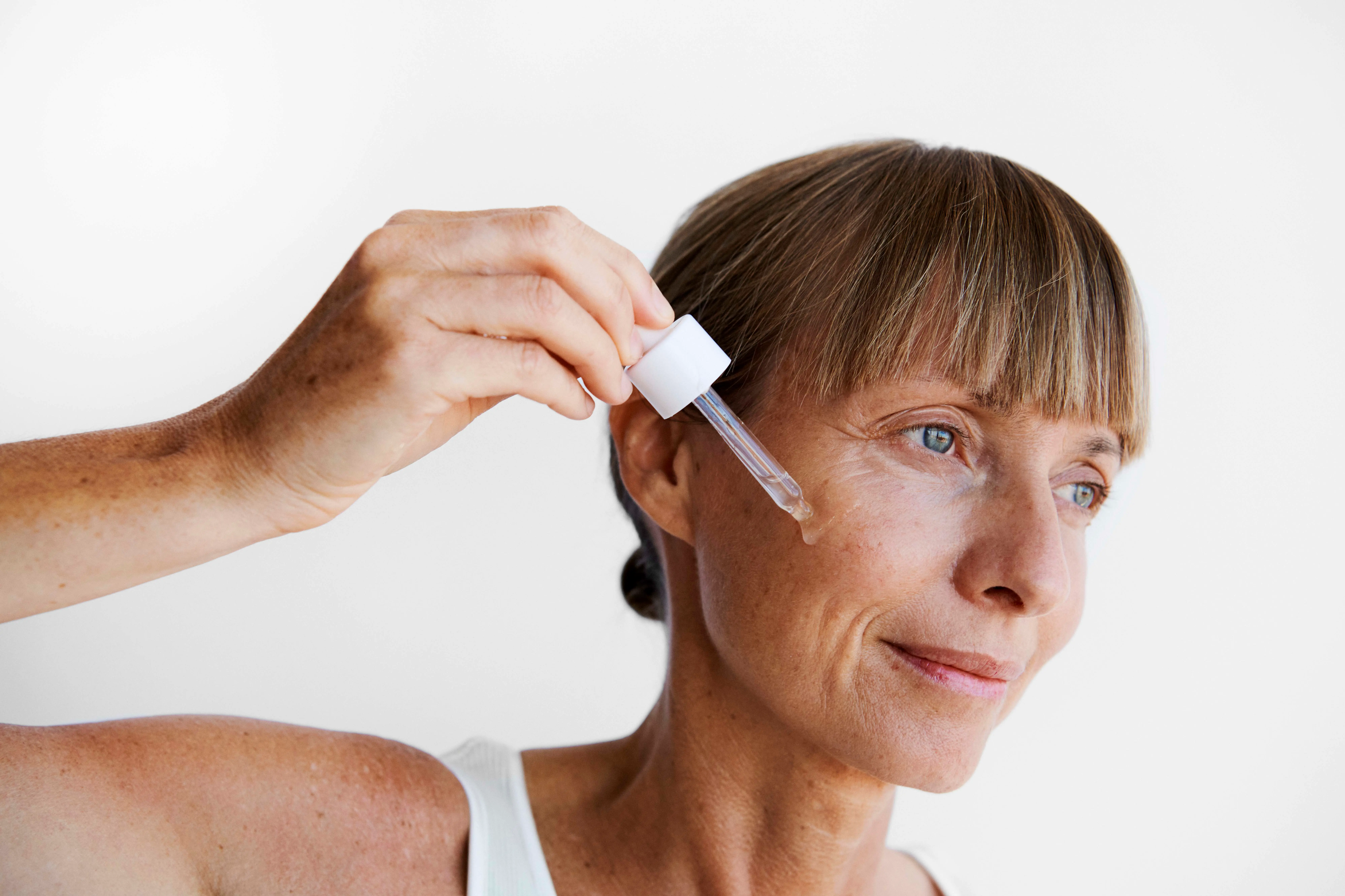 En kvinde drypper serum på sin kind med en pipette.