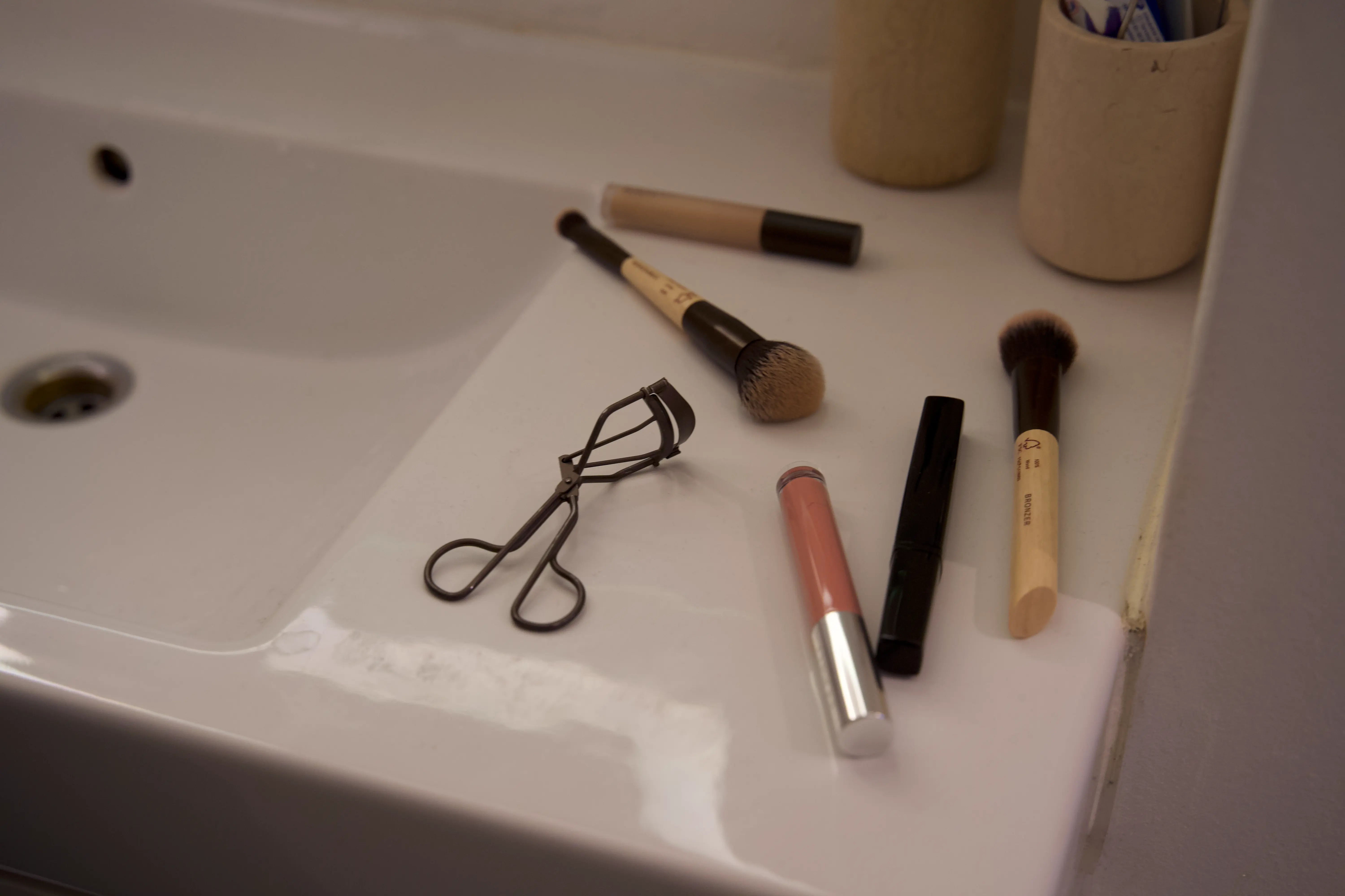 Makeup og makeupbørster ligger på en håndvask.