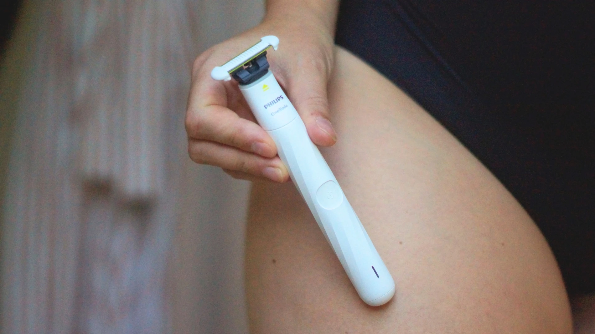 En hånd holder en hvid Philips OneBlade shaver mod et ben.