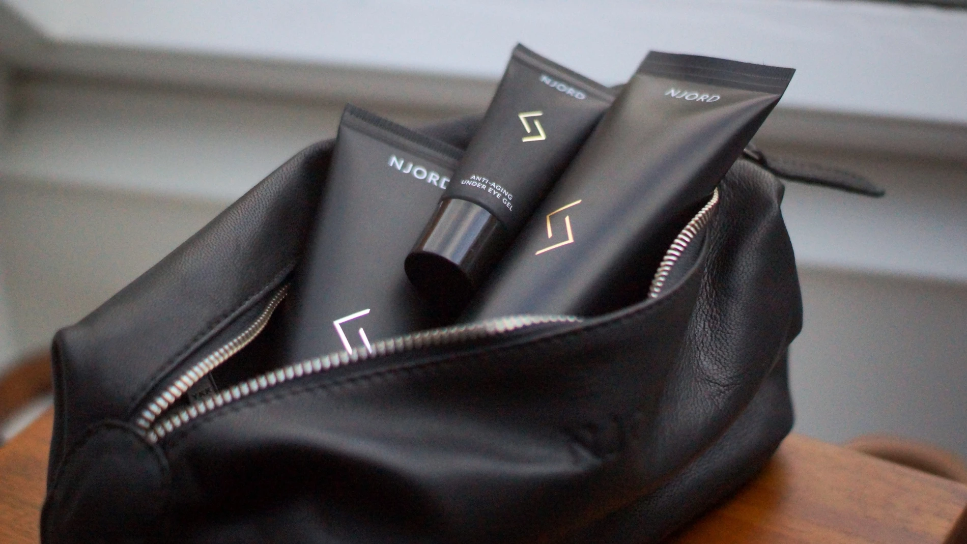 Tre sorte NJORD hudplejetuber, inklusive en Anti-Aging Under Eye Gel, i en åben sort lædertaske med lynlås.