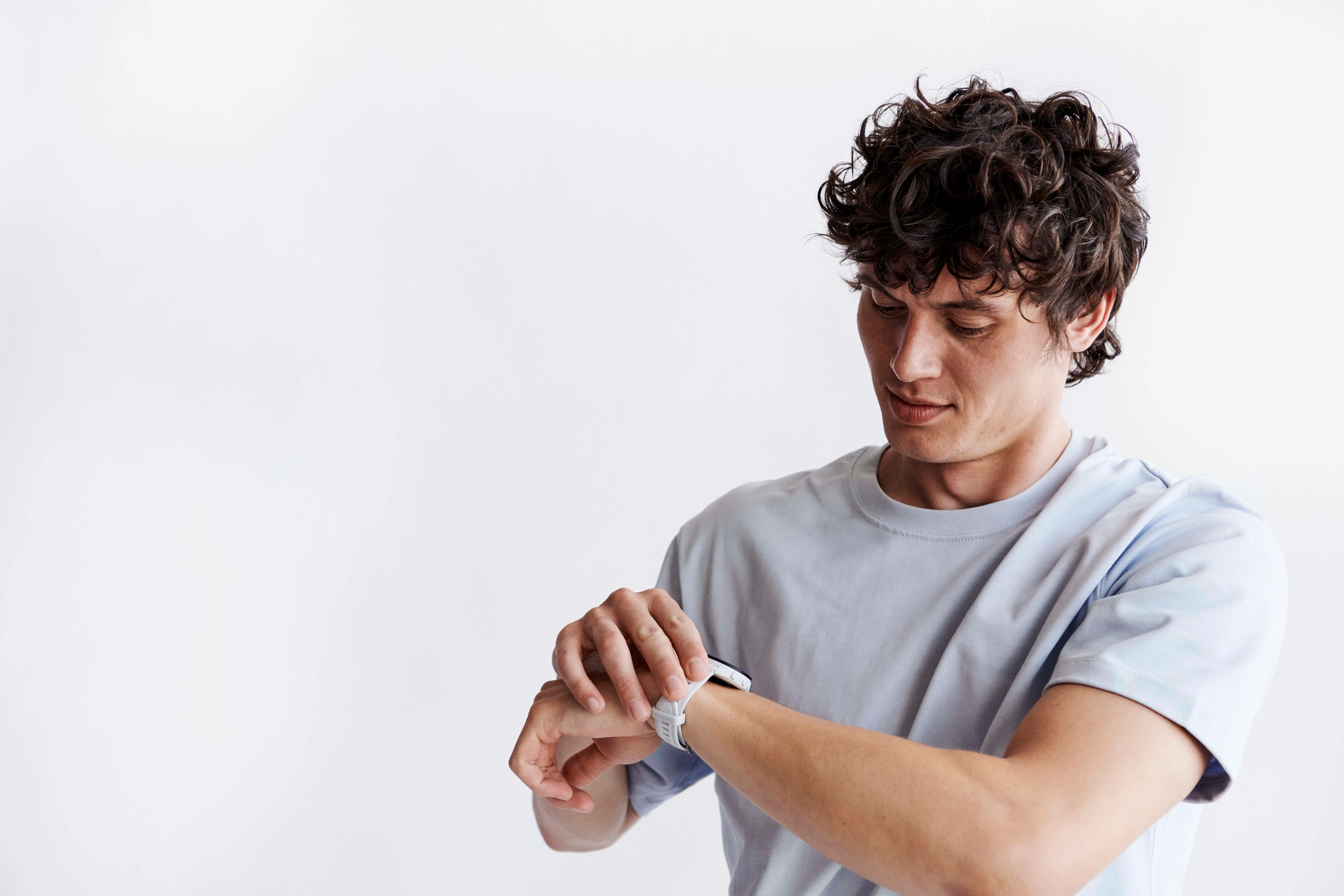 En mand med krøllet hår kigger på og interagerer med et hvidt smartwatch på sit håndled.