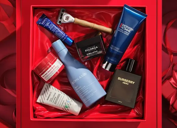 Bild som visar flera skönhetsprodukter arrangerade i en röd presentförpackning. Produkterna inkluderar en blå tub med Kiehl's Eye Fuel, en rakhyvel från Bulldog, en svart burk med Filorga Global-Repair, en blå tub med Biotherm Homme Force Supreme Body Reshaper, en svart flaska med Burberry Hero parfym, en blå flaska med Björn Axén Repair Shampoo, en vit tub med Matas Men Ansiktskräm, och en röd burk med Recipe for Men Ultra Soft Beard Balm. Bakgrunden är röd.