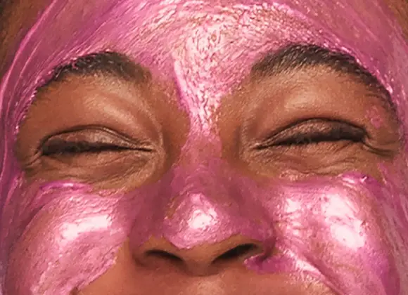 Leende person applicerar en glittrig rosa ansiktsmask.