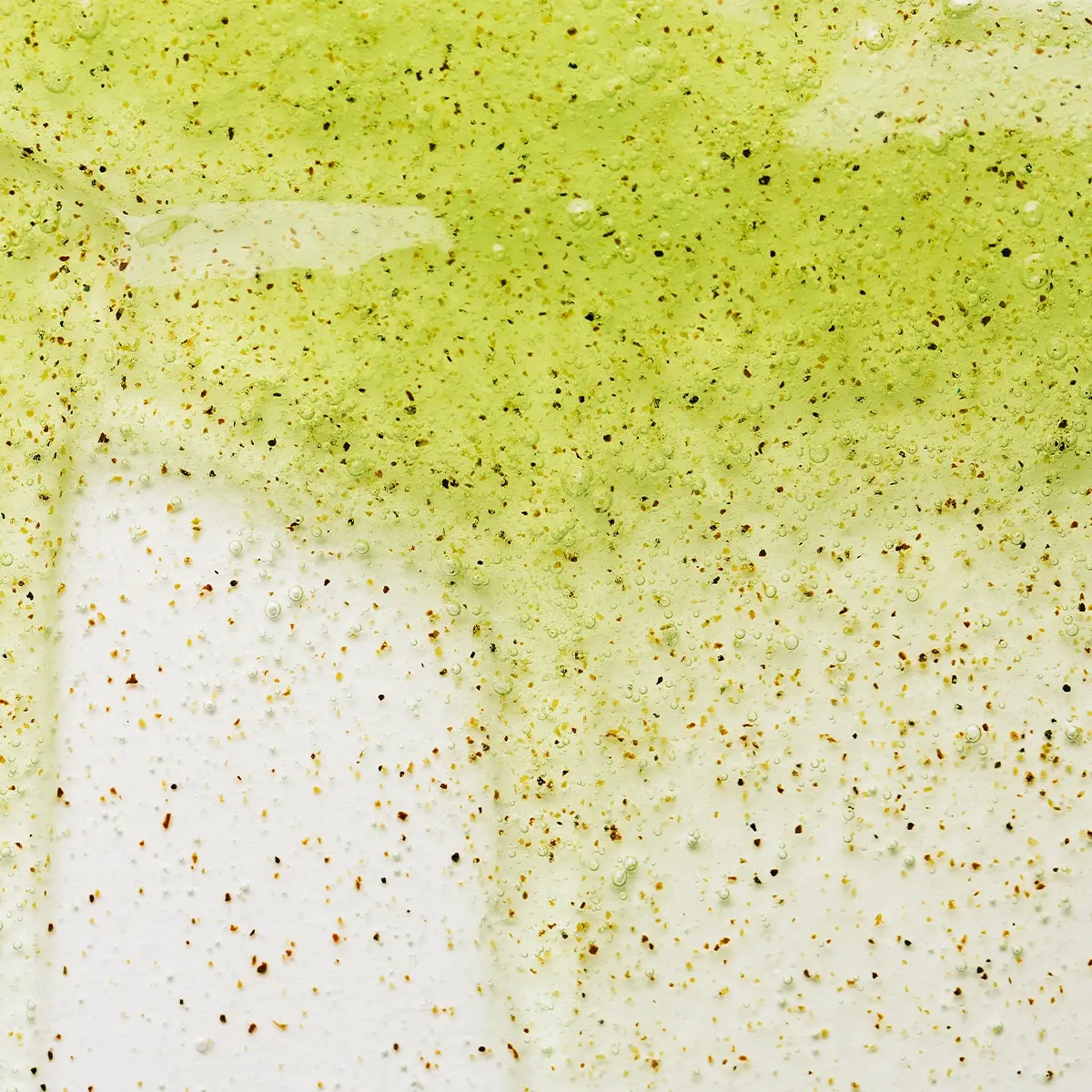 Närbild av en ljusgrön hudvårdsprodukt med små exfolierande korn och en krämig, lätt skummande textur. Detaljbild som framhäver peelingens konsistens och ingredienspartiklar.