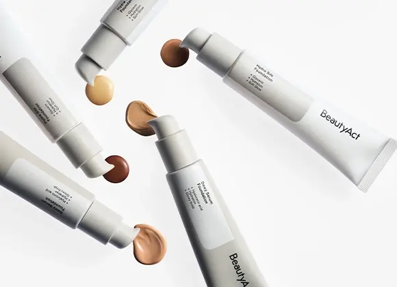 Bild som visar olika foundationprodukter från BeautyAct. I bilden syns fem tuber med olika nyanser av foundation, inklusive ljus, medium och mörk. Varje tub har en pump som släpper ut en liten mängd foundation. Produkterna är arrangerade i en cirkel på en vit bakgrund.